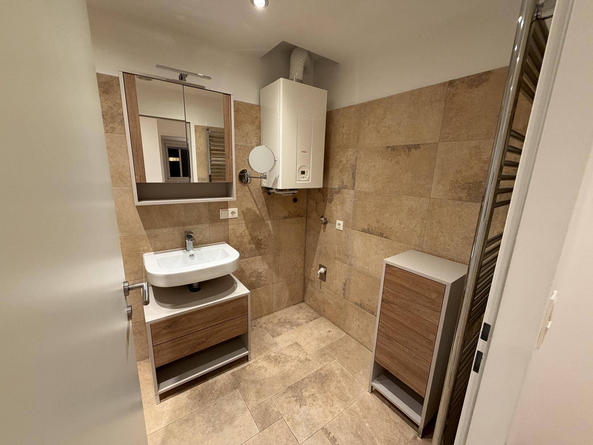 Modernes Badezimmer mit Waschbecken, Spiegelschrank und Wandheizkörper, komplett gefliest.