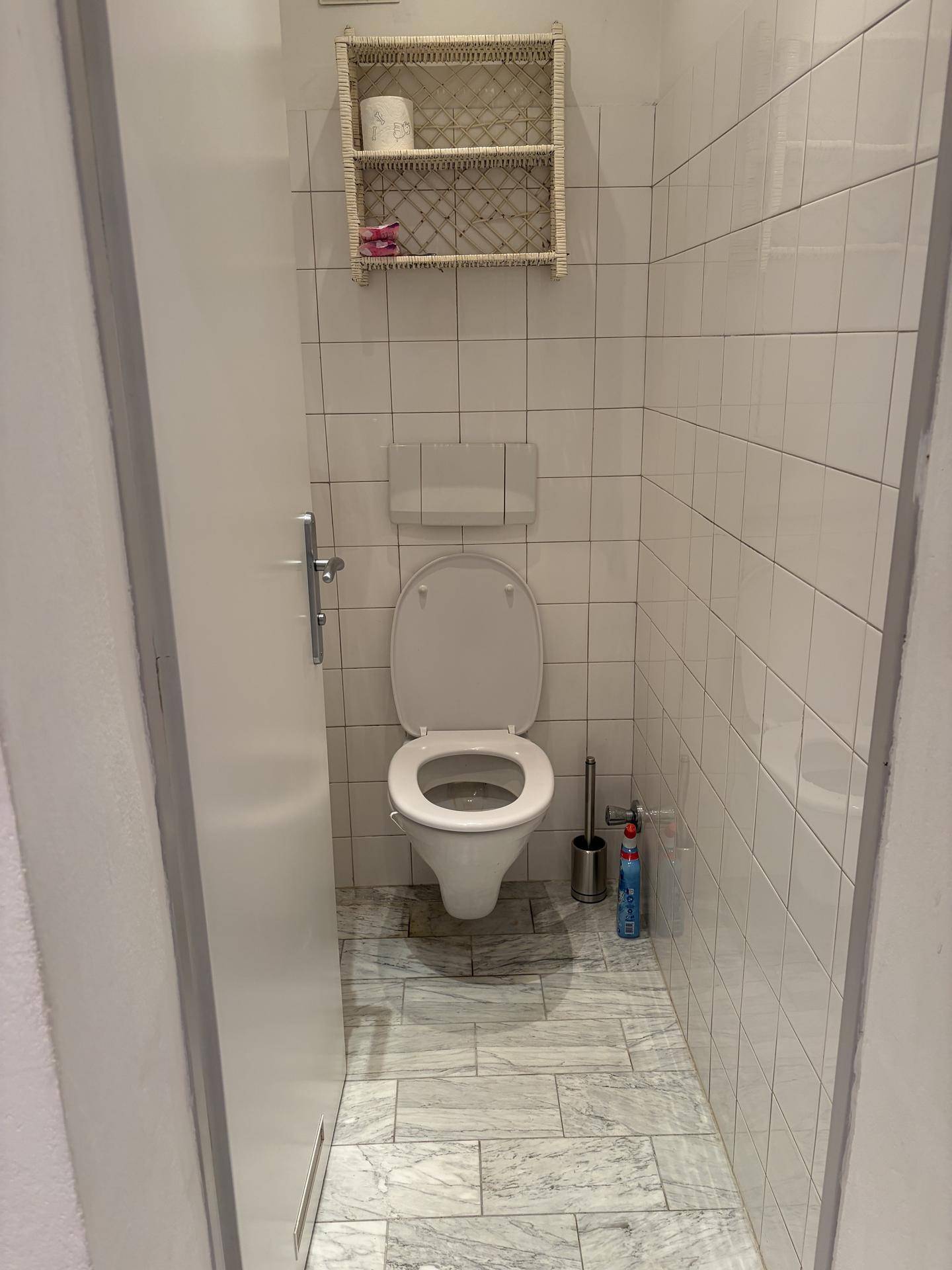 Kleines Gäste-WC mit weiß gefliesten Wänden und einfacher Toilette.