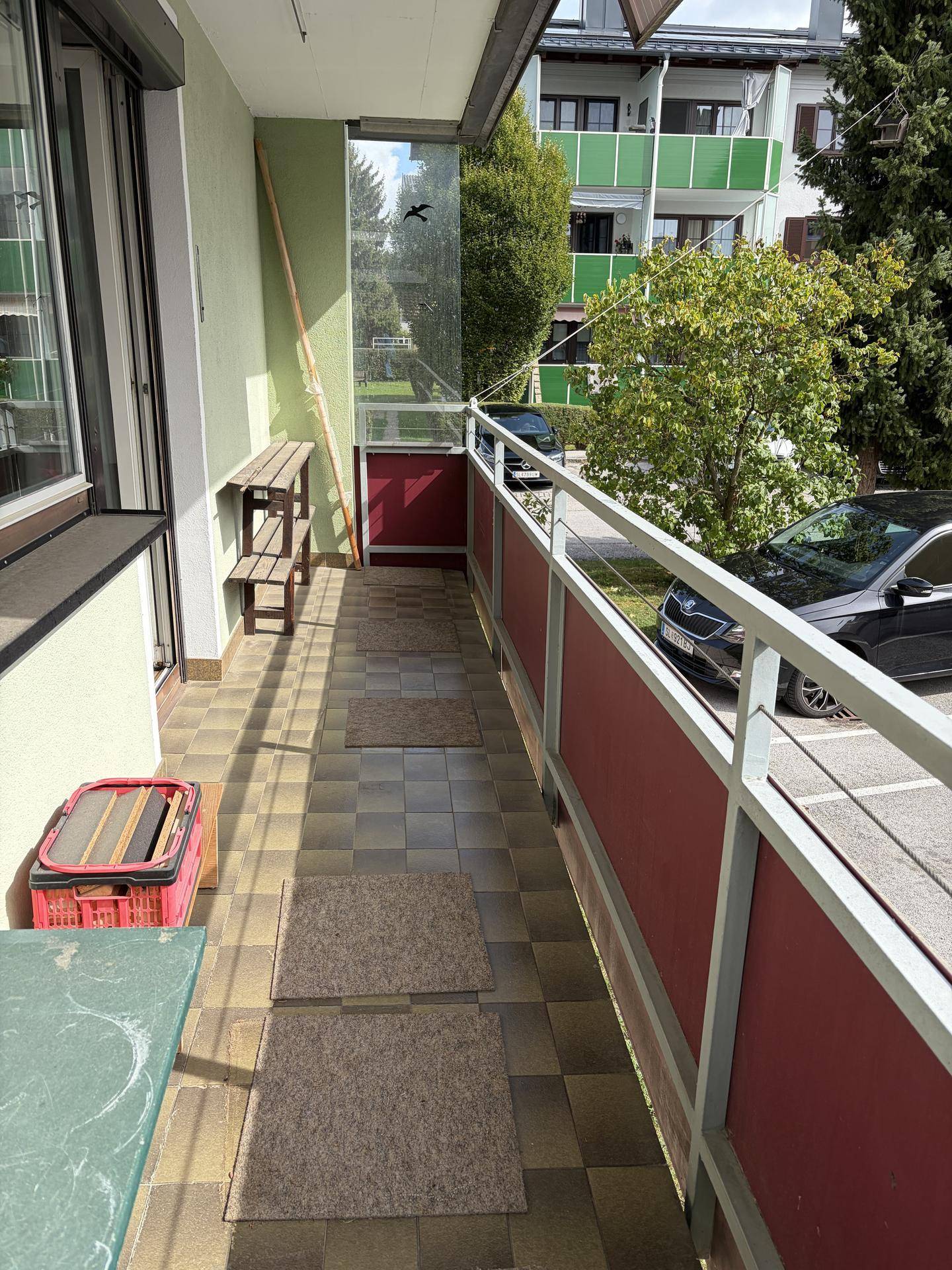 Langer Balkon mit Fliesenboden und Blick auf die Straße und Bäume.