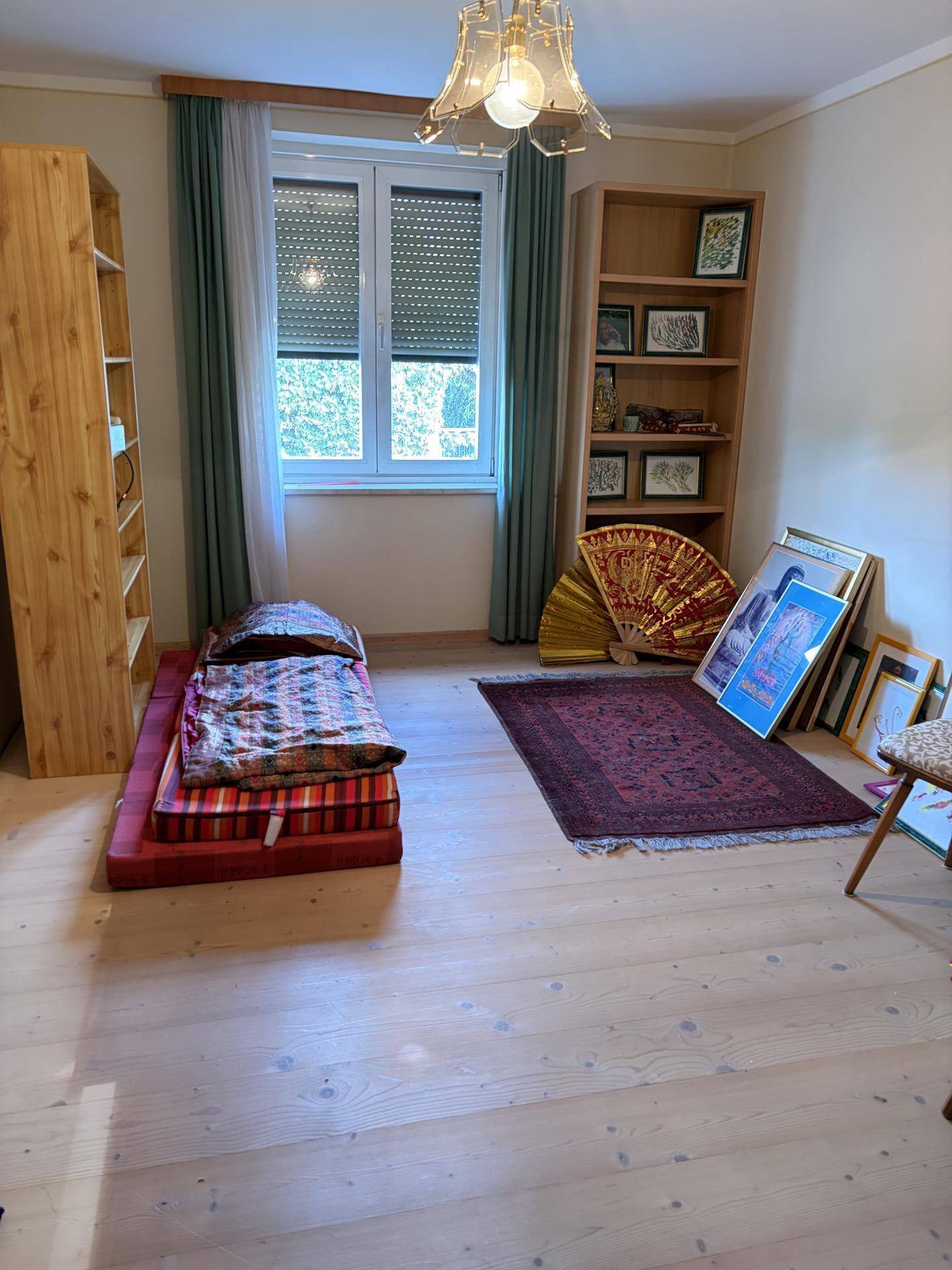 Helles Schlafzimmer mit Holzboden, Fenster und einfacher Einrichtung.