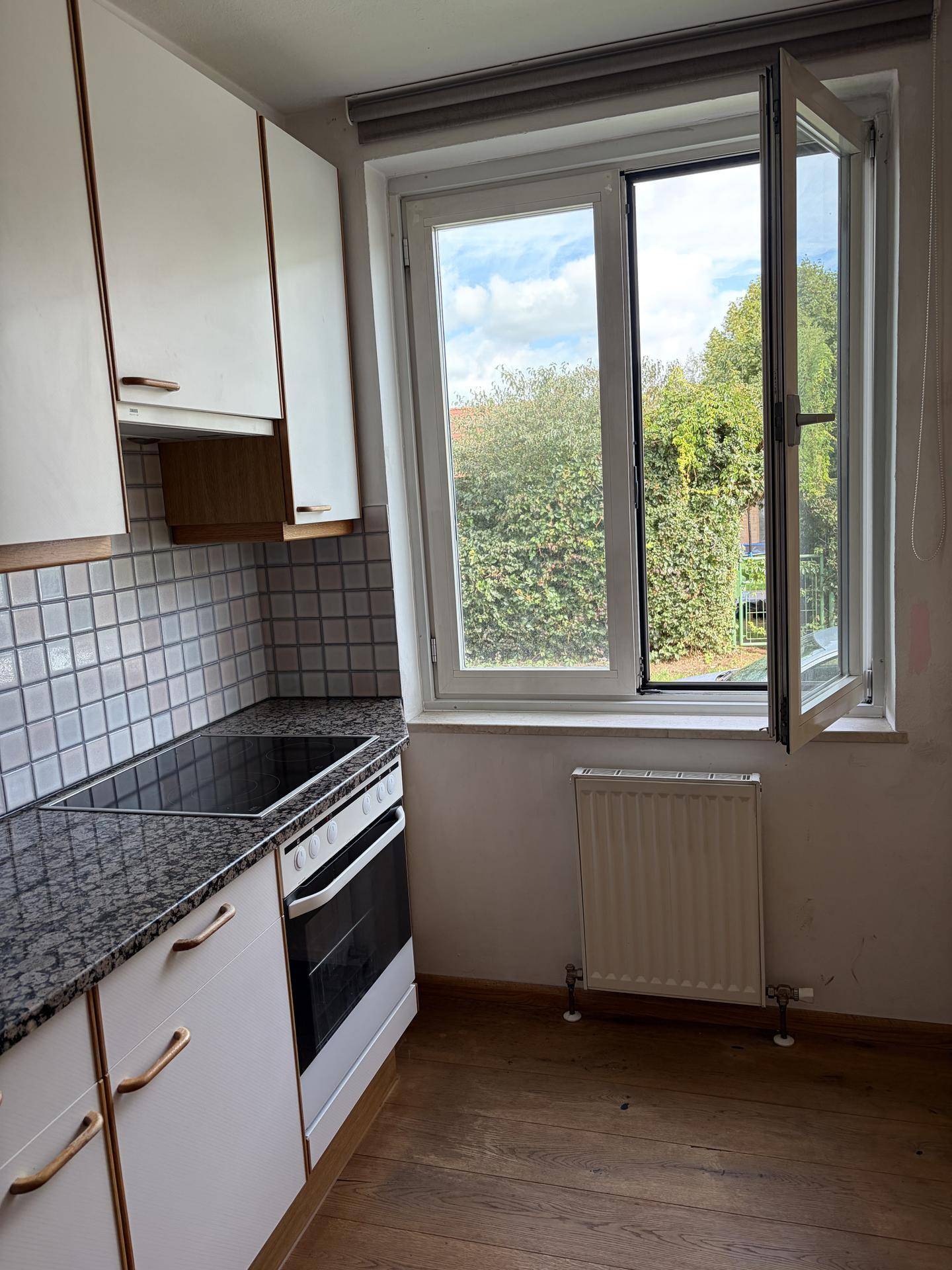 Funktionale Küche mit weißen Schränken, Granitarbeitsplatte und Fensterblick ins Grüne.