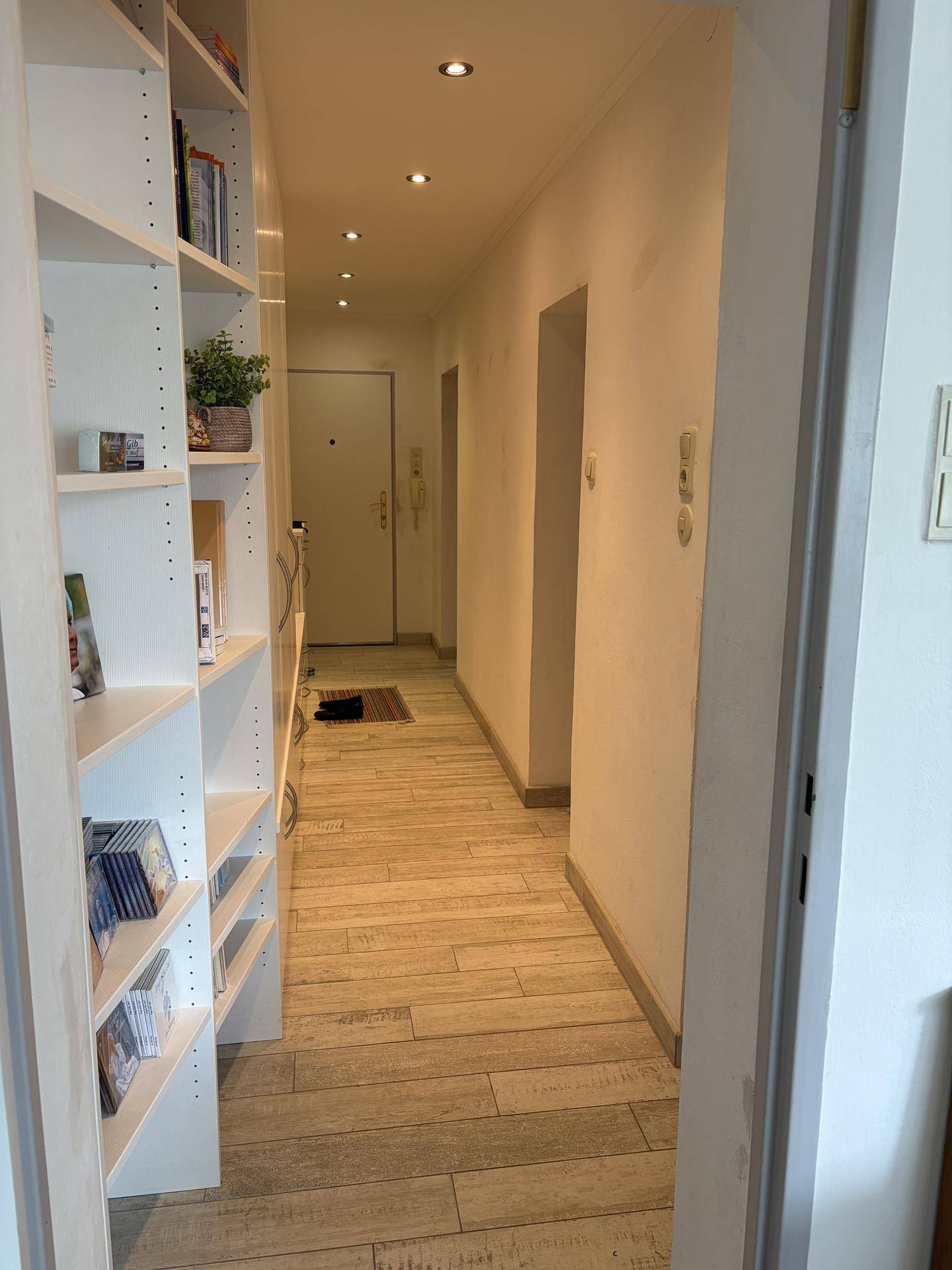 Heller Flur mit Bücherregal, Einbaustrahlern und hellem Holzfußboden.
