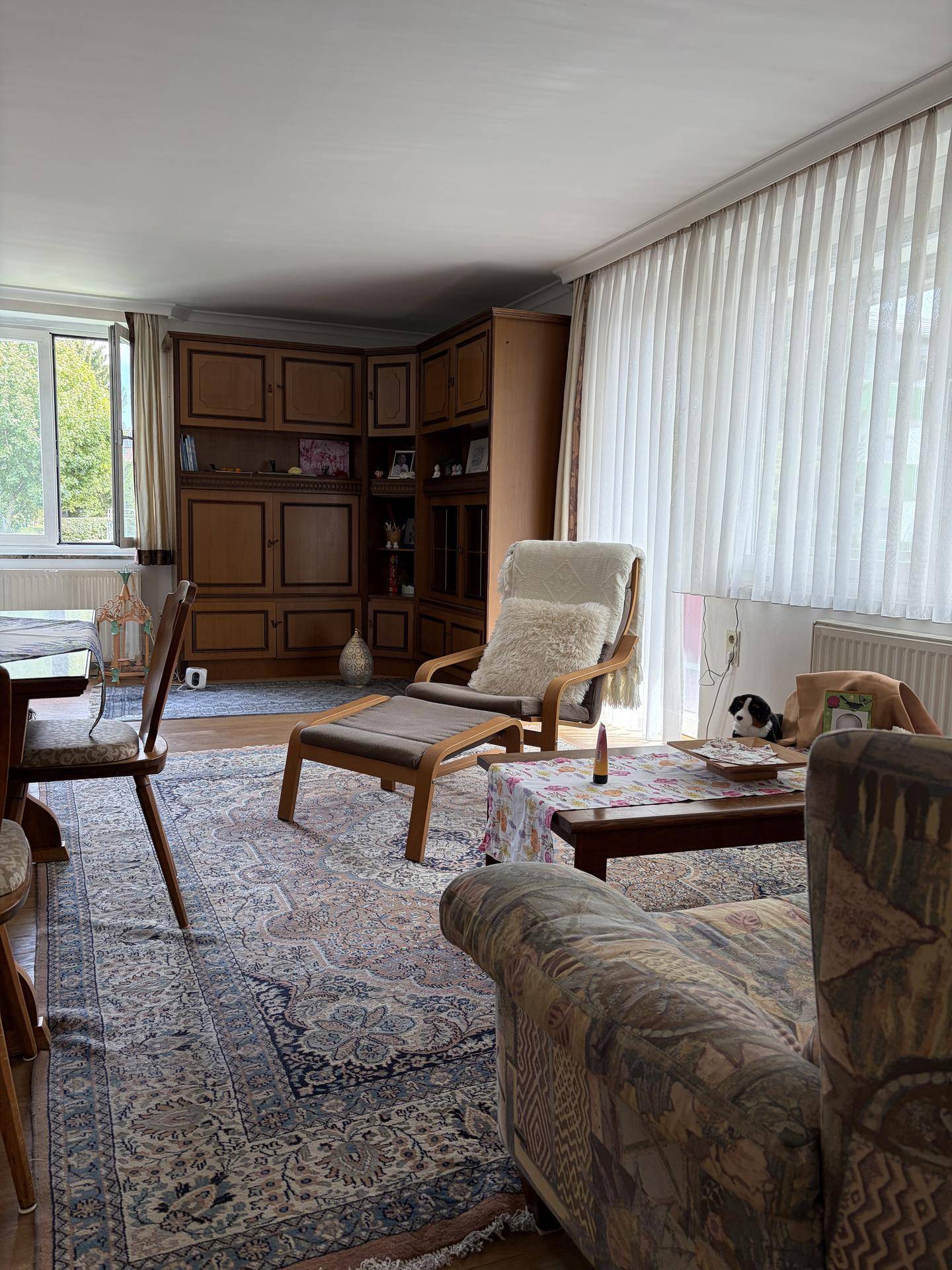 Geräumiger Wohnbereich mit großem Fenster, Teppich und traditionellen Möbeln.