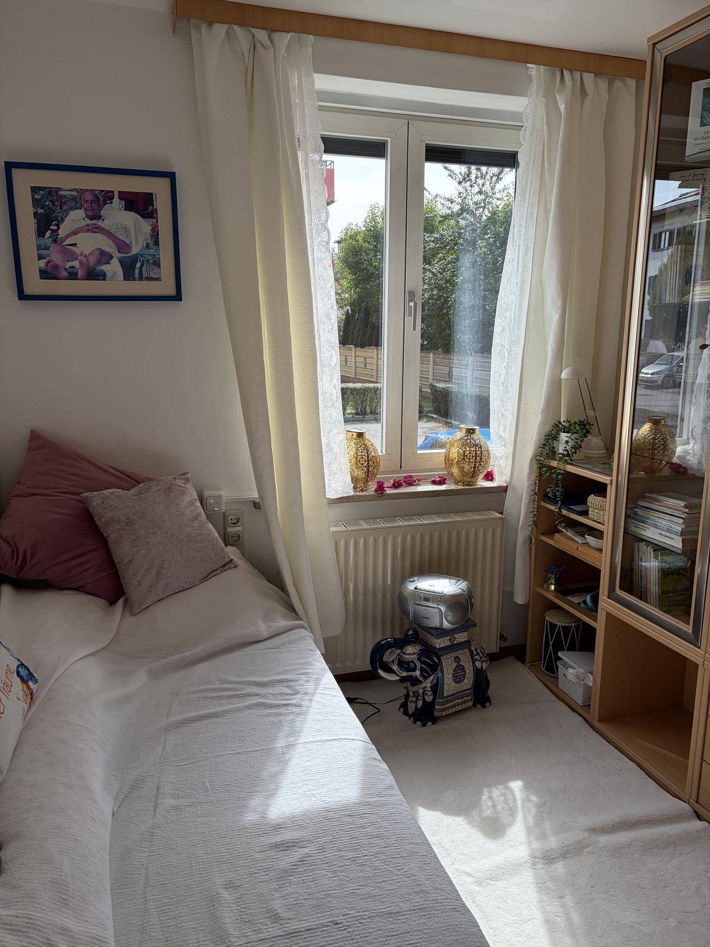 Helles Schlafzimmer mit Einzelbett, Fenster und Bücherregal.