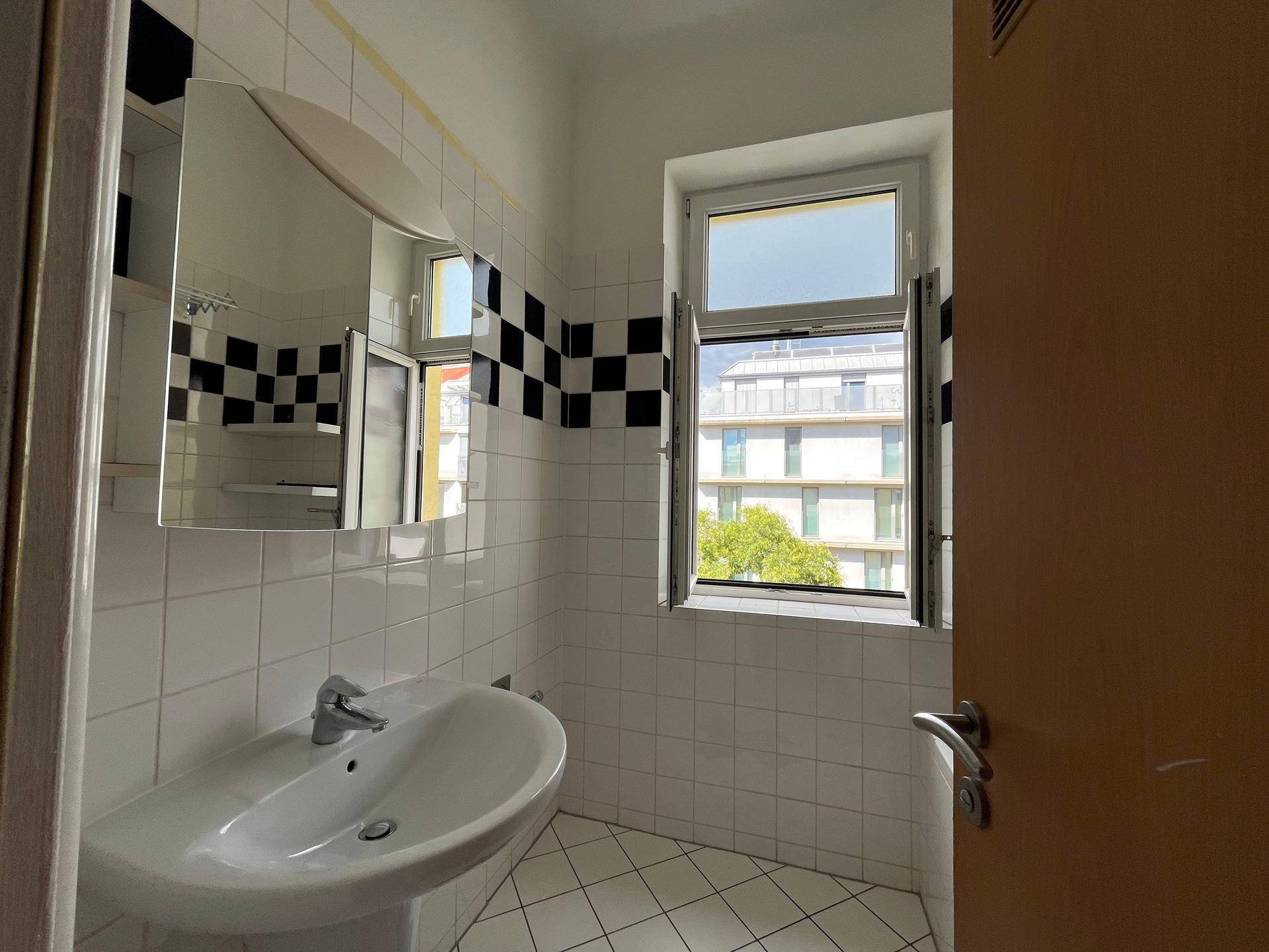 Helles Badezimmer mit Waschbecken, Spiegelschrank und Blick aus dem Fenster auf die Umgebung.