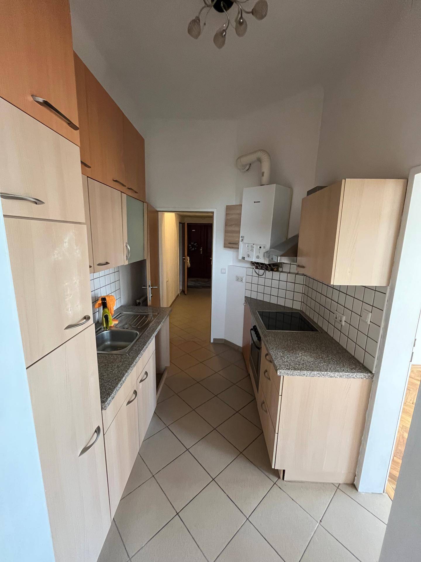 Schmale Küche mit beidseitigen Schränken, Fliesenboden und Blick in den Flur.