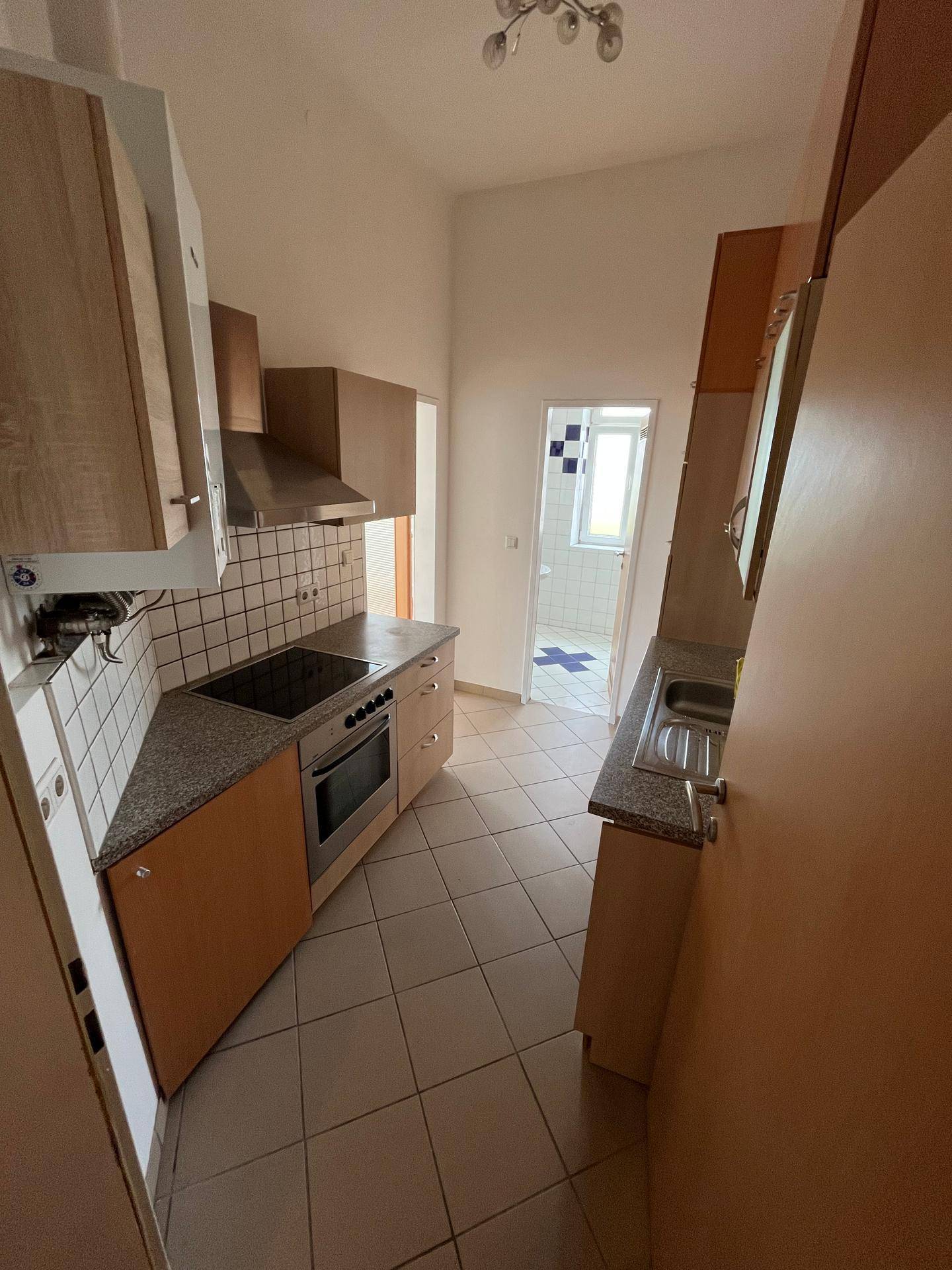 Funktionale Küche mit Kochfeld, Backofen und Zugang zu einem weiteren Raum.