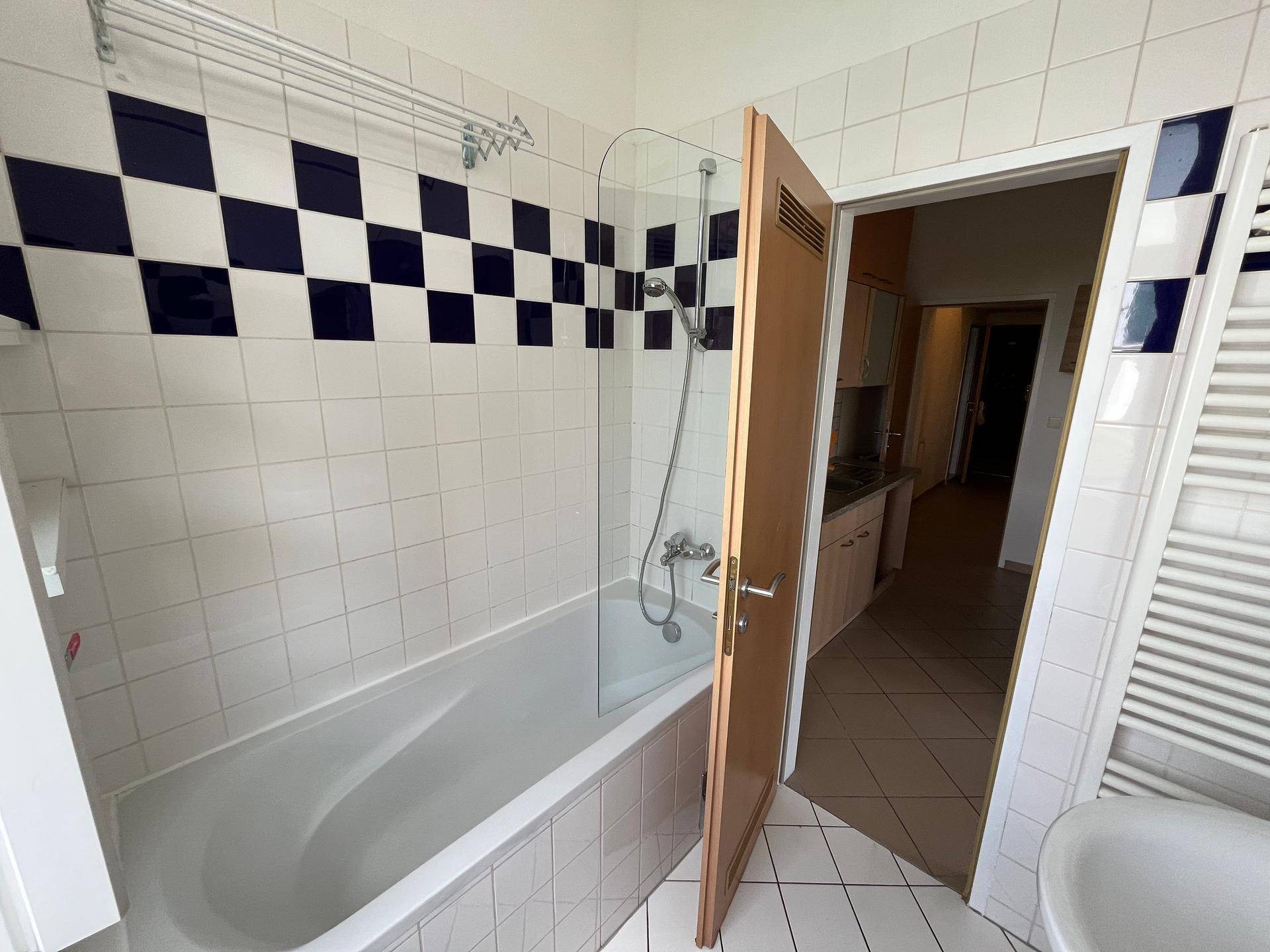 Badezimmer mit Badewanne und Blick in die angrenzende Küche durch die offene Tür.