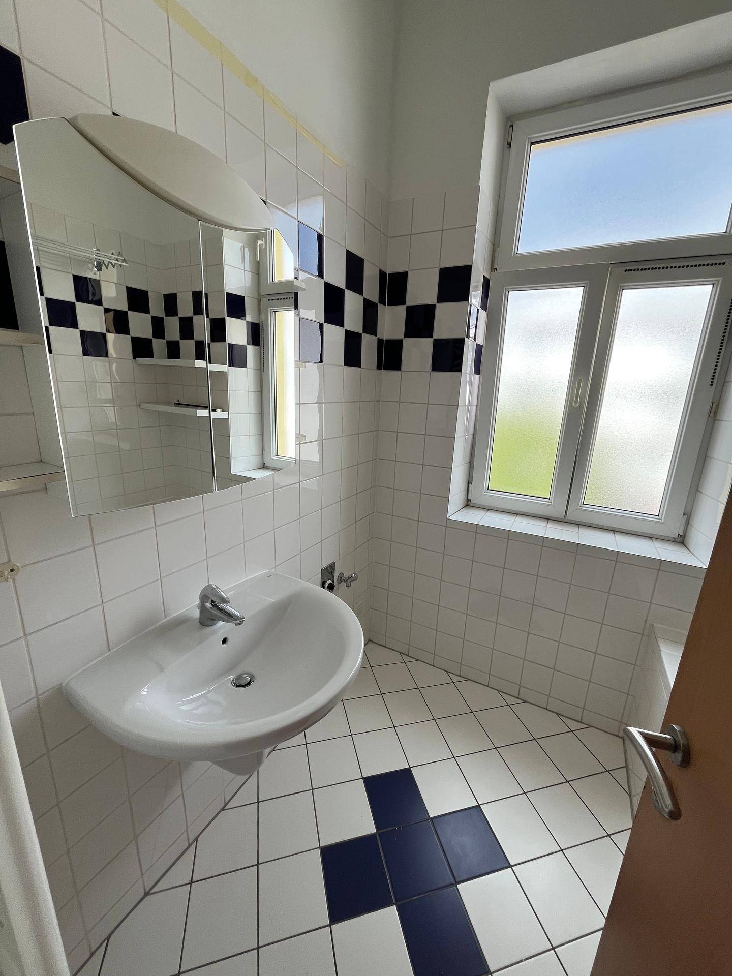 Badezimmer mit Waschbecken, Spiegelschrank und Fenster, das Tageslicht hereinlässt.