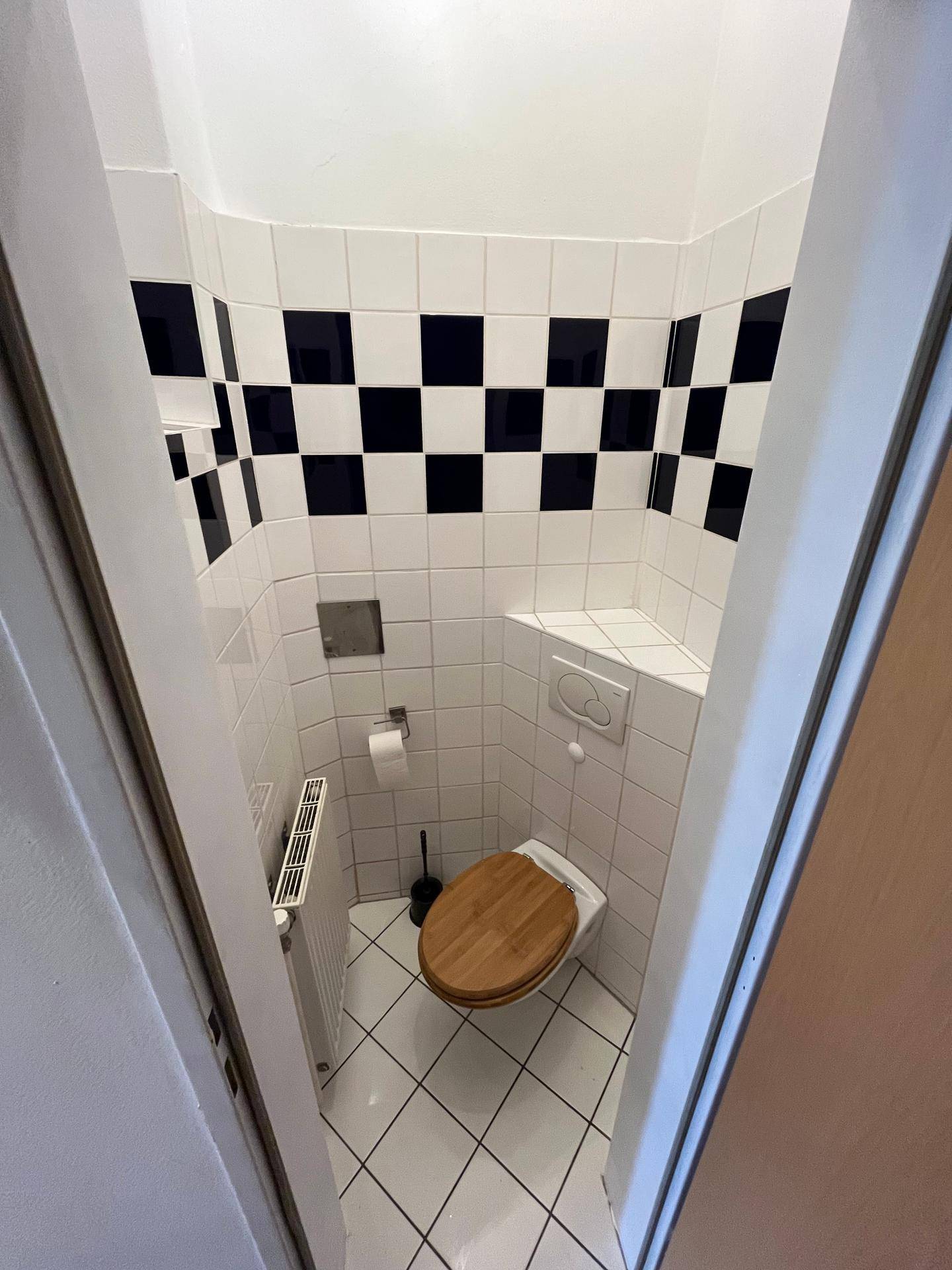 Kleines Gäste-WC mit schwarz-weiß gefliesten Wänden und Holzsitz auf der Toilette.