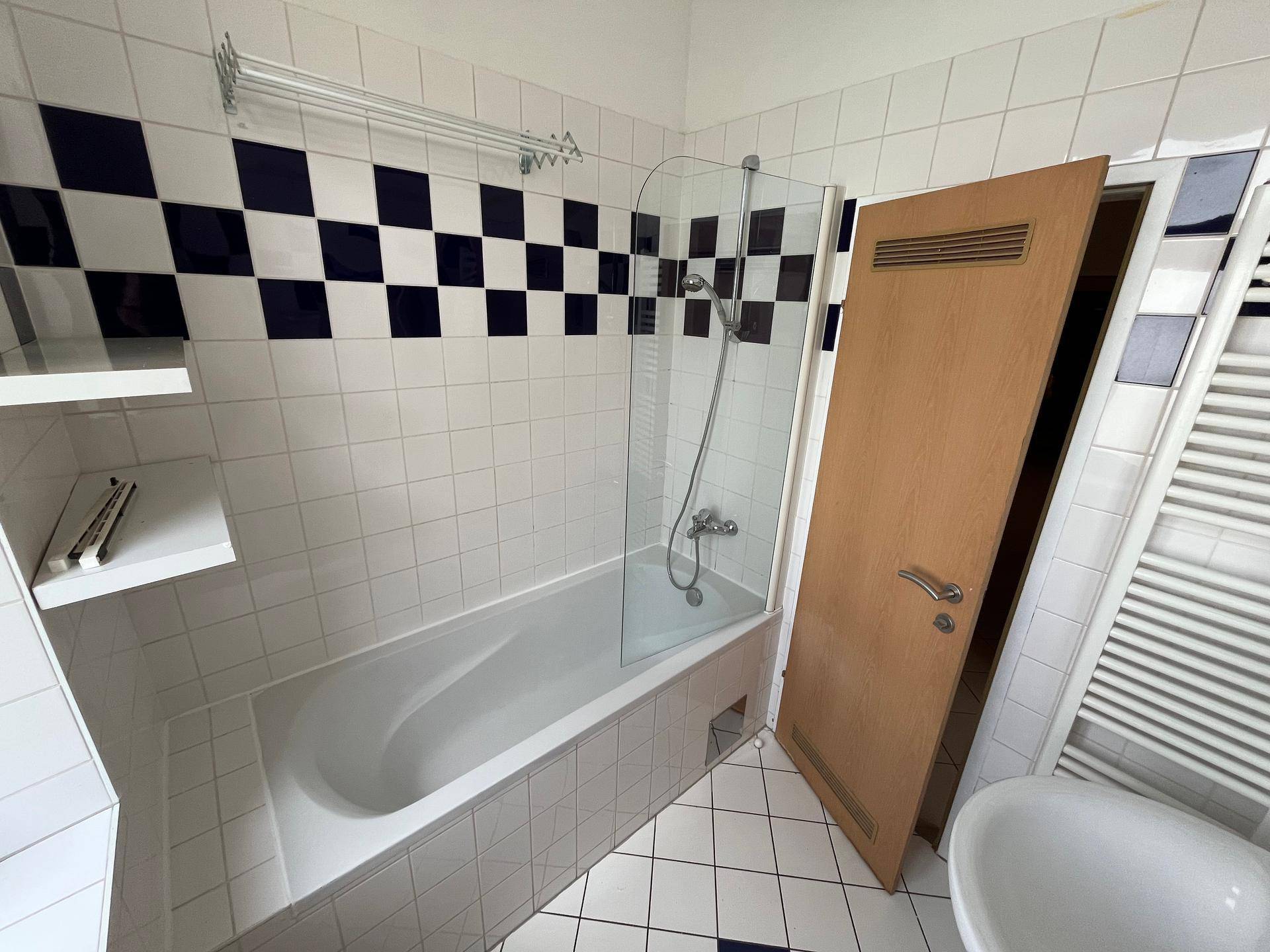 Badezimmer mit Badewanne, Duschabtrennung und Handtuchheizkörper an der Wand.