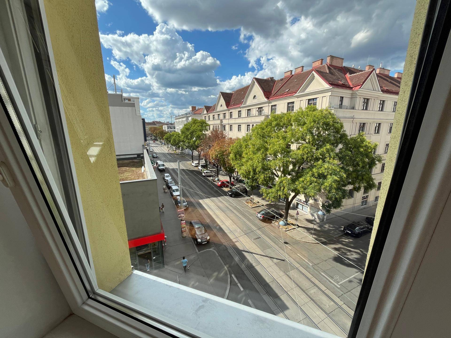 Blick aus dem Fenster auf eine belebte Stadtstraße mit Gebäuden und Bäumen.