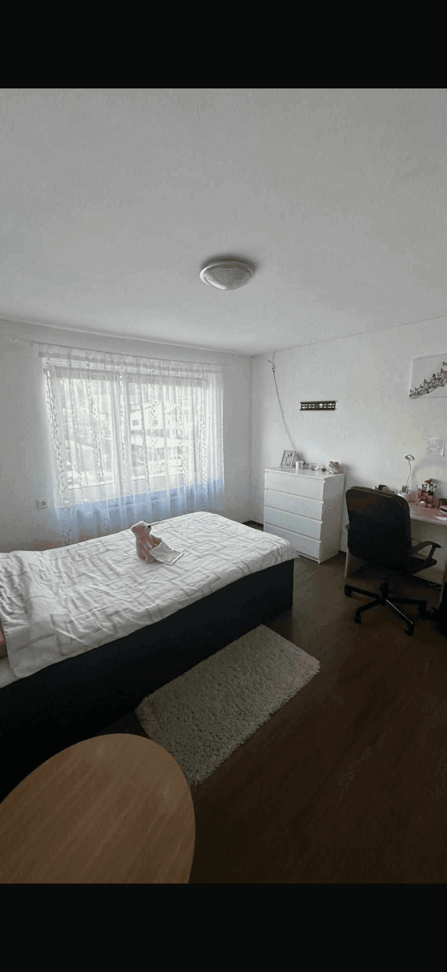 Gemütliches Schlafzimmer mit Bett, weißer Kommode und Schreibtisch, ausgestattet mit dunklem Holzboden.