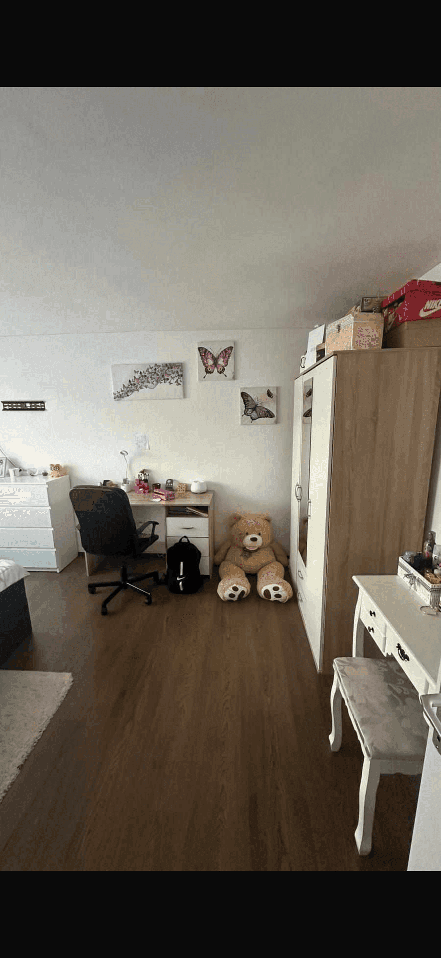 Schlafzimmer mit Schreibtisch, Kleiderschrank und dunklem Holzboden, dekoriert mit Schmetterlingsbildern.