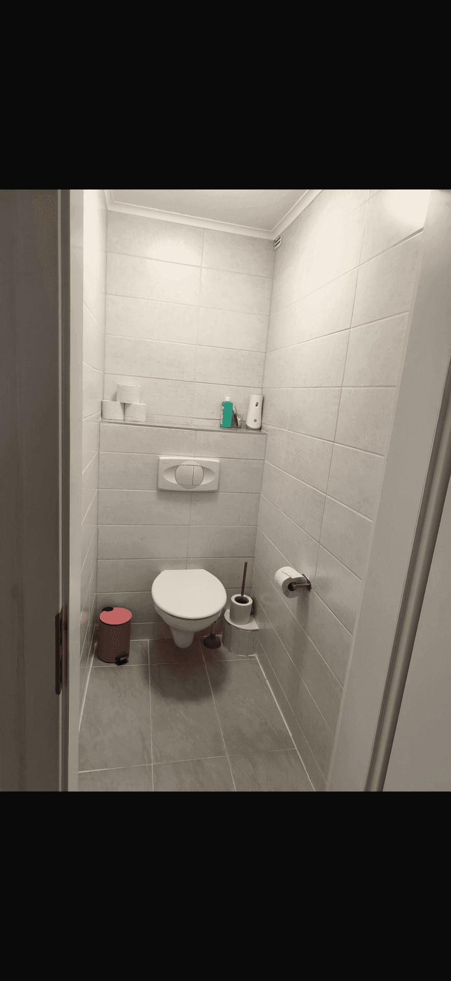 Kleines Gäste-WC mit hellgrauen Fliesen an Wänden und Boden sowie wandhängendem WC.