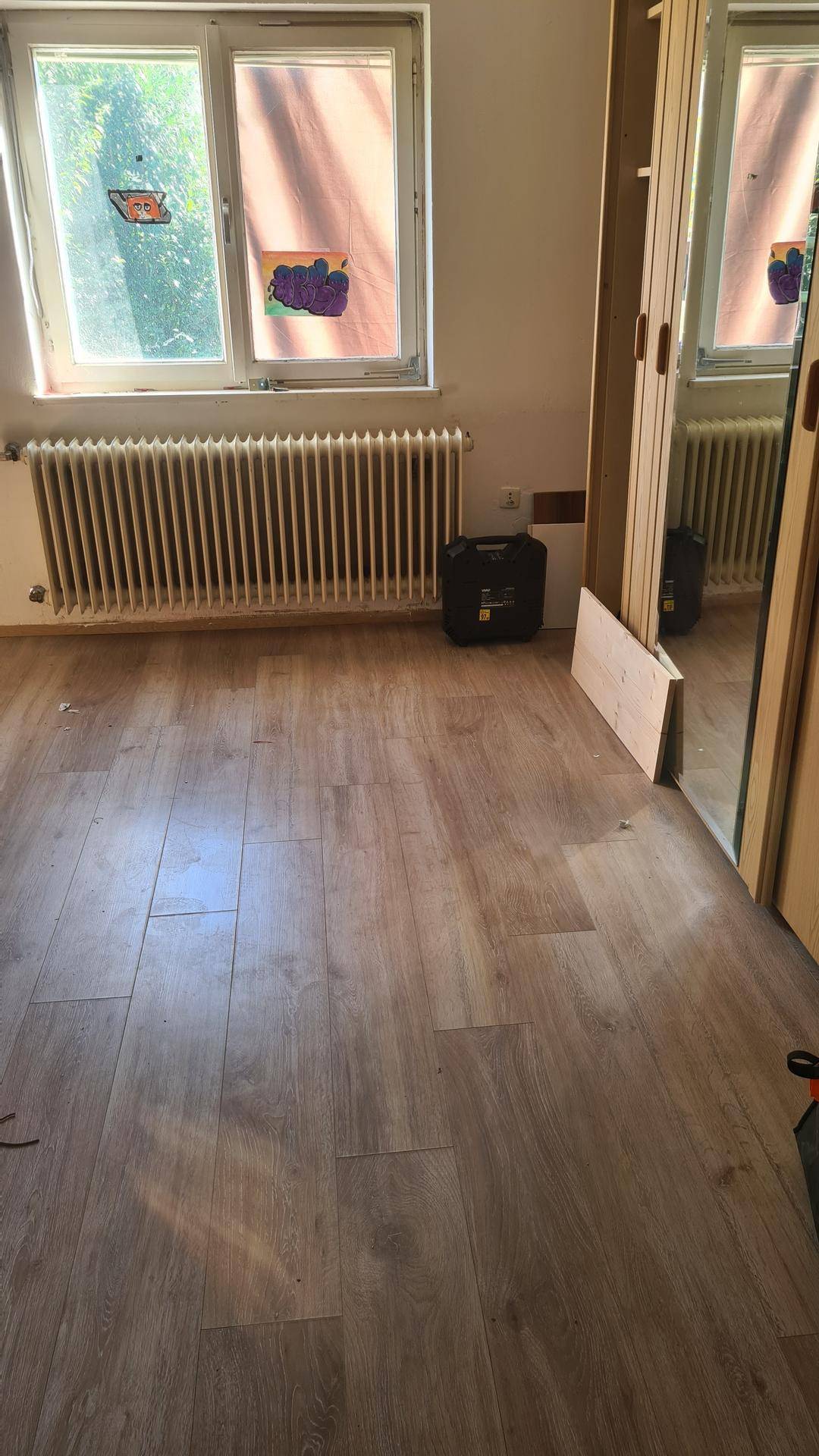 Heller Raum mit Holzboden, großem Fenster und Heizkörper.