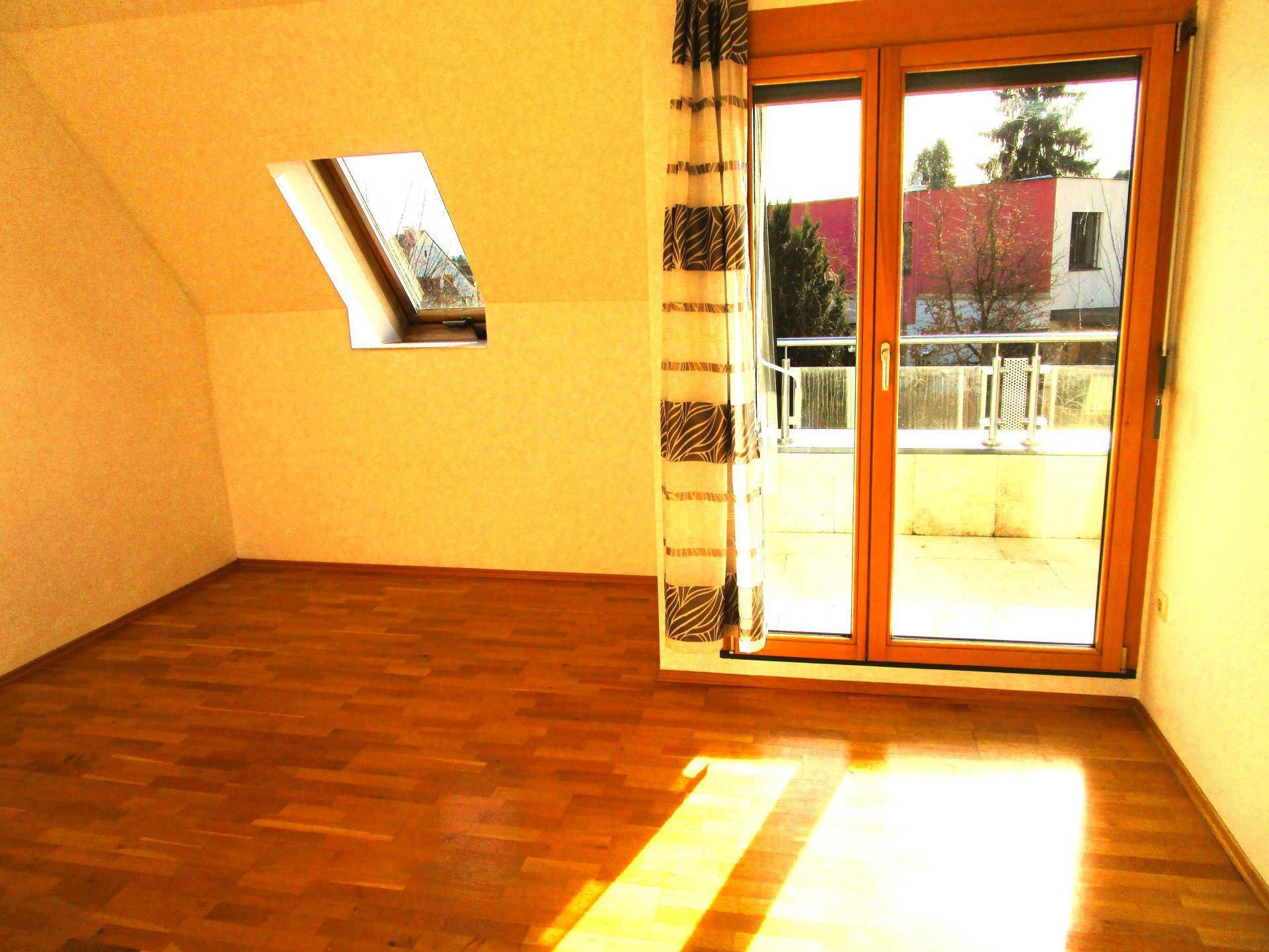 Helles Zimmer im Dachgeschoss mit Holzboden, Dachfenster und Zugang zu einem Balkon.