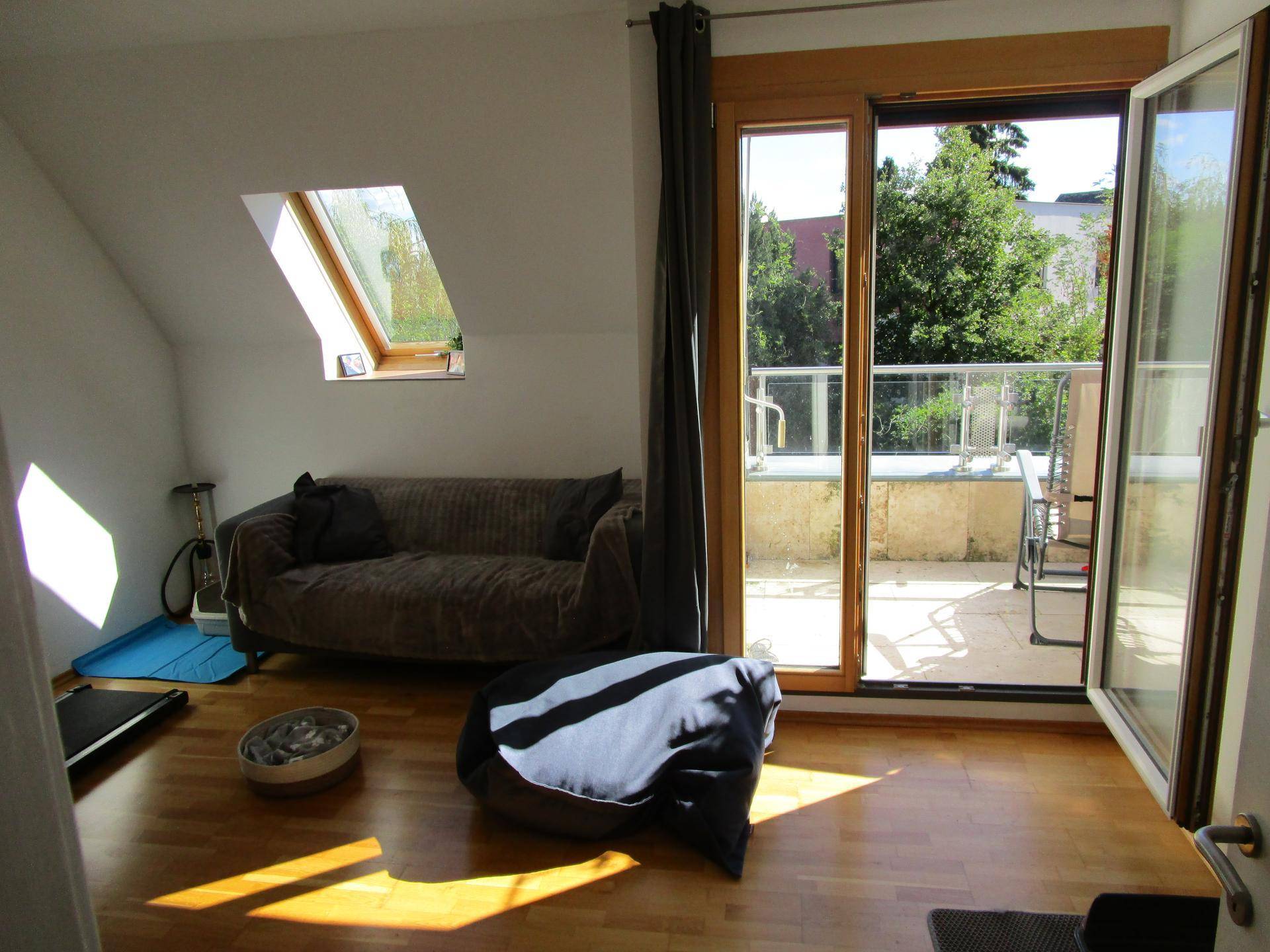 Heller Wohnraum im Dachgeschoss mit Holzboden, Dachfenster und direktem Zugang zur Terrasse.