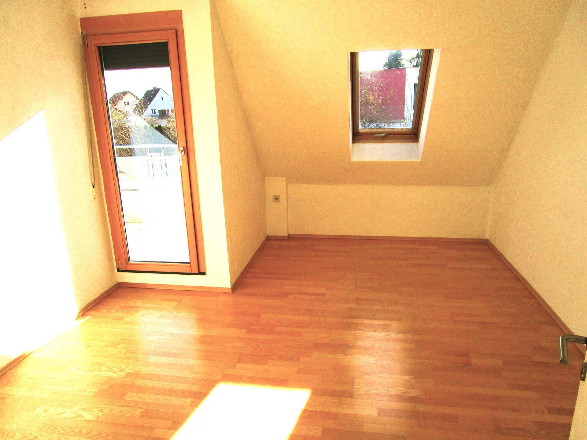 Geräumiges Dachzimmer mit Holzboden, Dachfenster und Balkontür, hell und einladend.