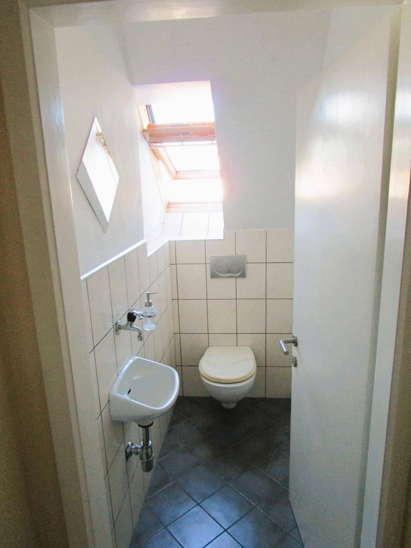 Kleines Gäste-WC mit weißen Fliesen, wandhängendem WC und einem Dachfenster.