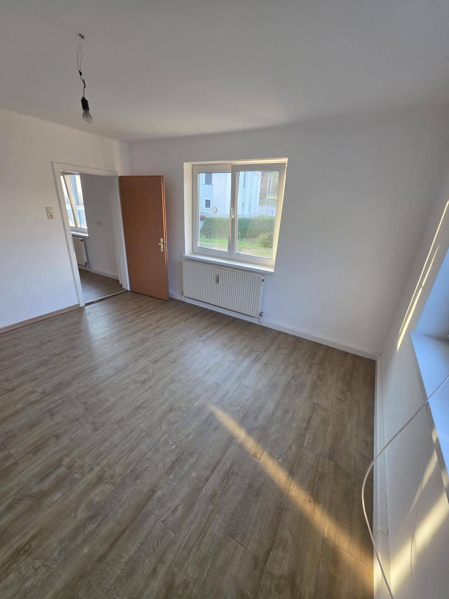 Lichtdurchfluteter, leerer Raum mit Laminatboden und einem großen Fenster, das viel Helligkeit bietet.
