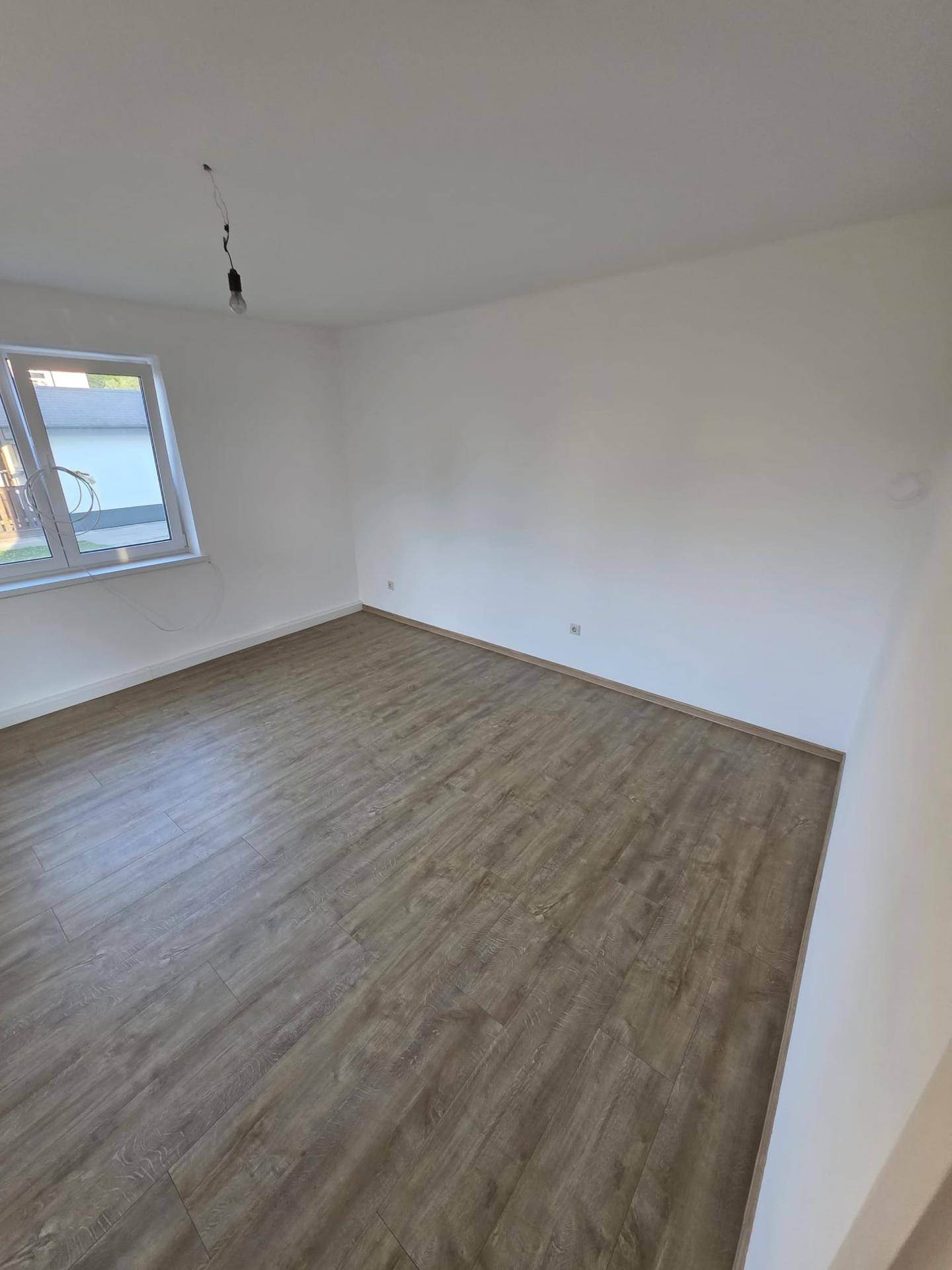 Geräumiger, leerer Raum mit hellem Laminatboden und weißen Wänden, ideal für ein Schlafzimmer.