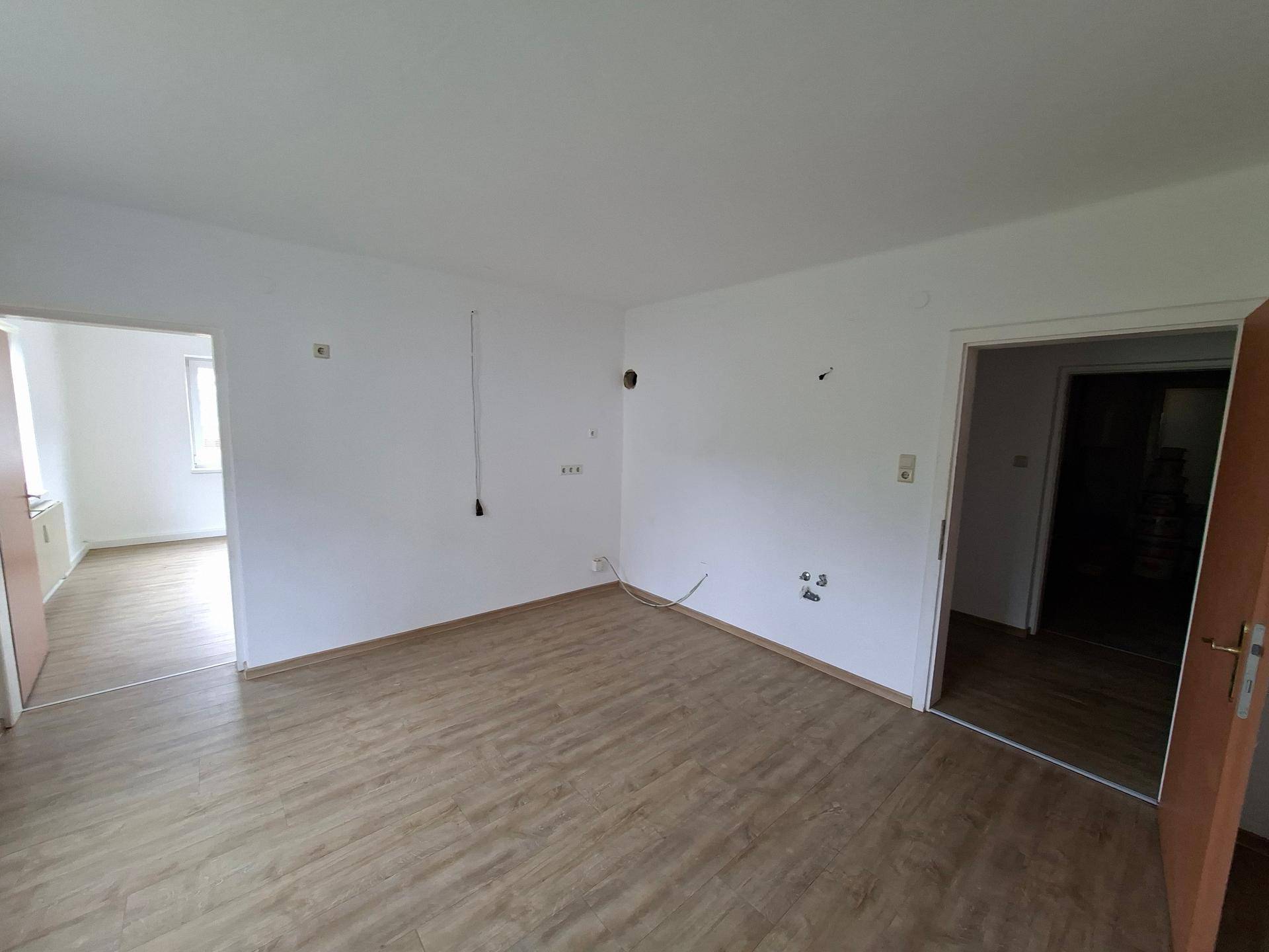 Leerer Raum mit hellem Laminatboden und weißen Wänden, bereit für die individuelle Gestaltung.