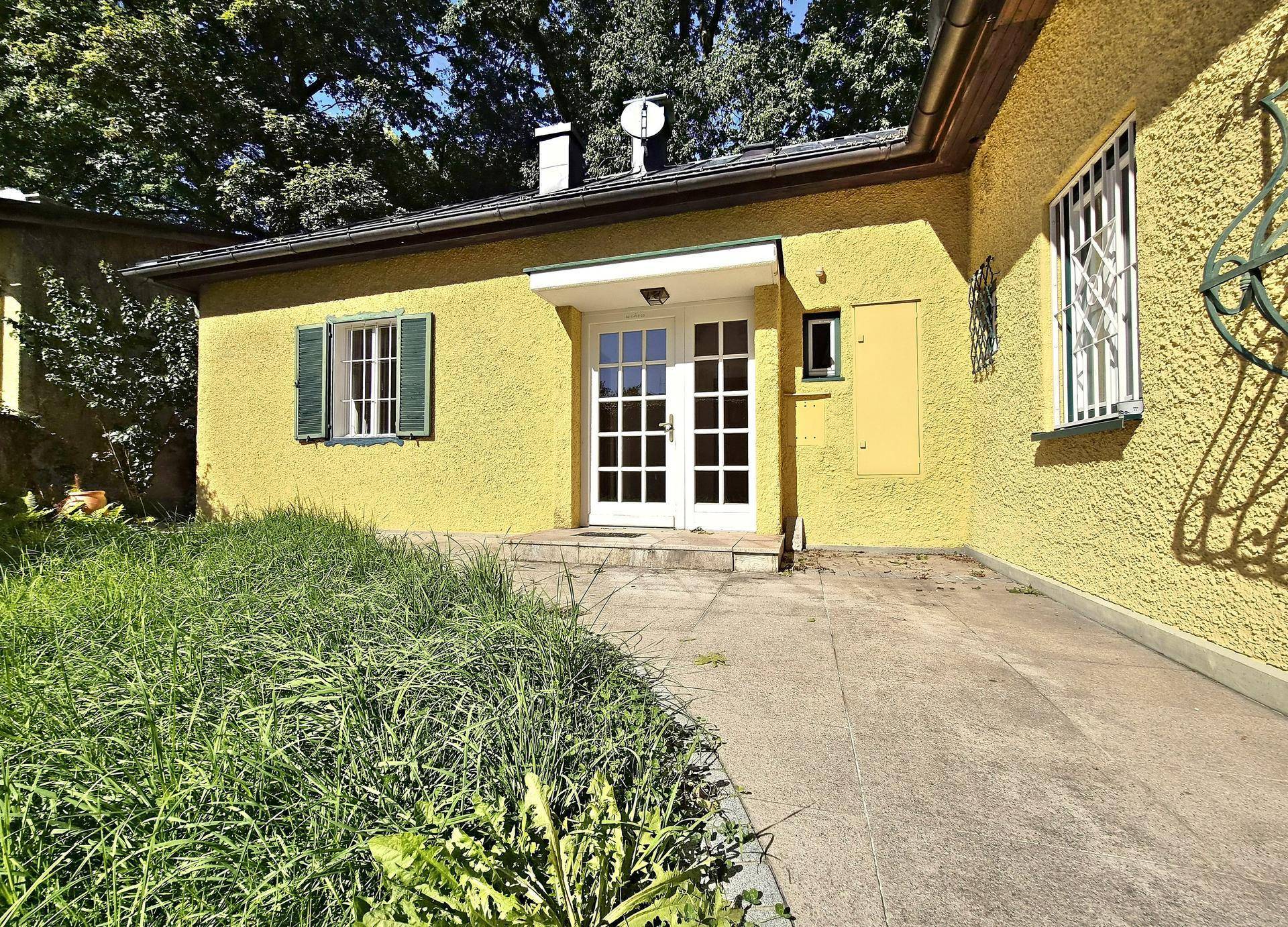 Hinterhof mit einer gepflasterten Terrasse, Rasenfläche und französischen Türen, die ins Haus führen.