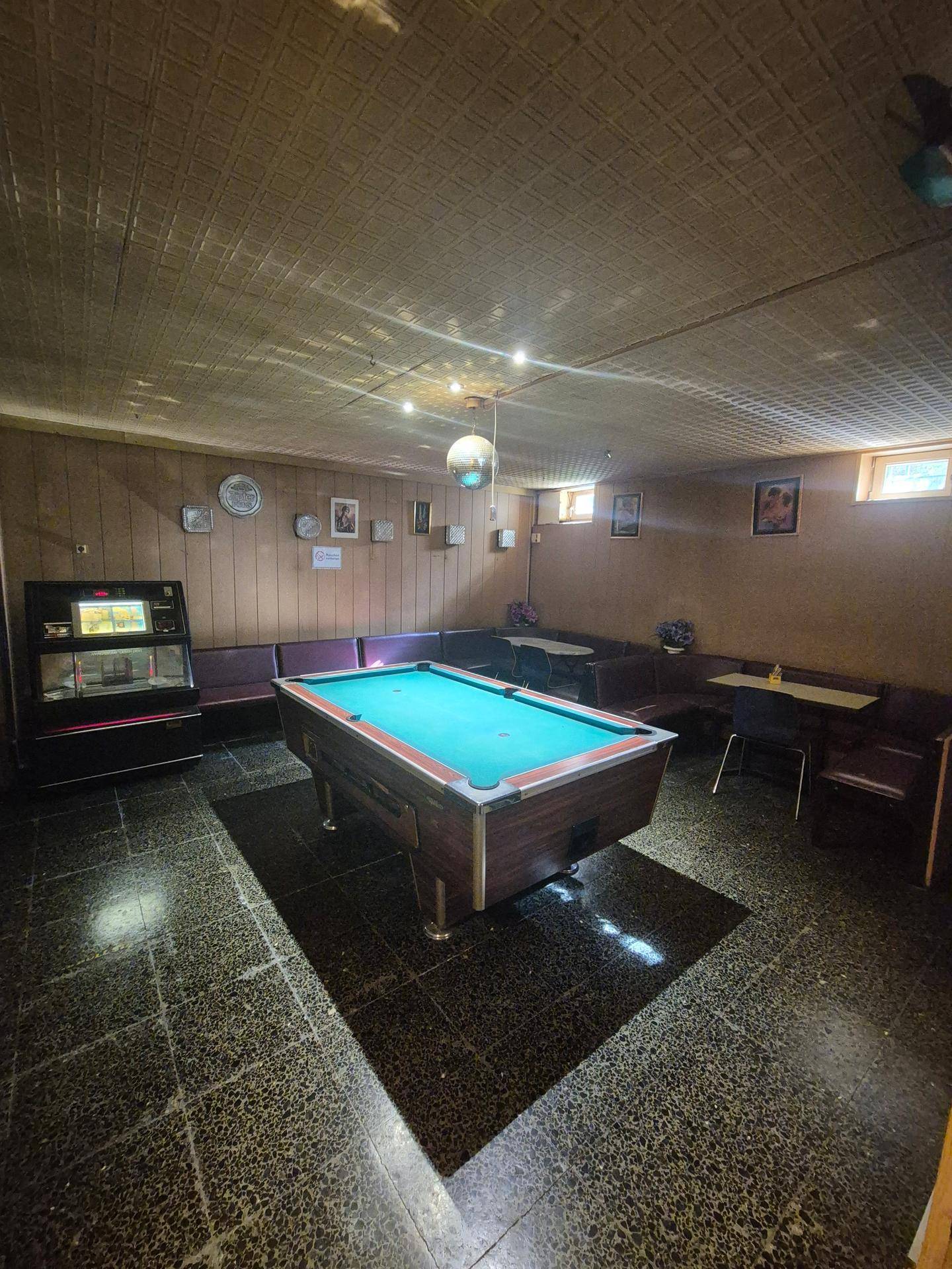 Geräumiger Spielraum mit Billardtisch, Jukebox und dunklem Fliesenboden, ideal für Unterhaltung.