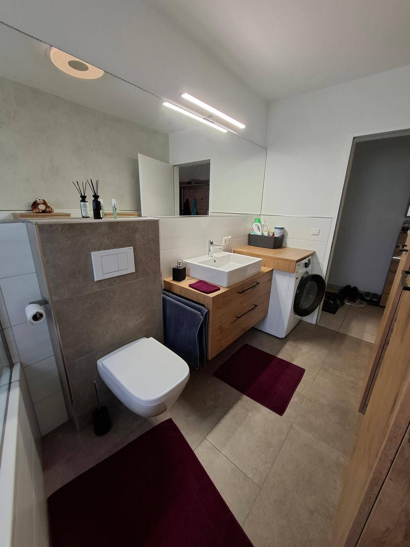 Helles Badezimmer mit Waschbecken, WC und integrierter Waschmaschine unter dem Spiegel.