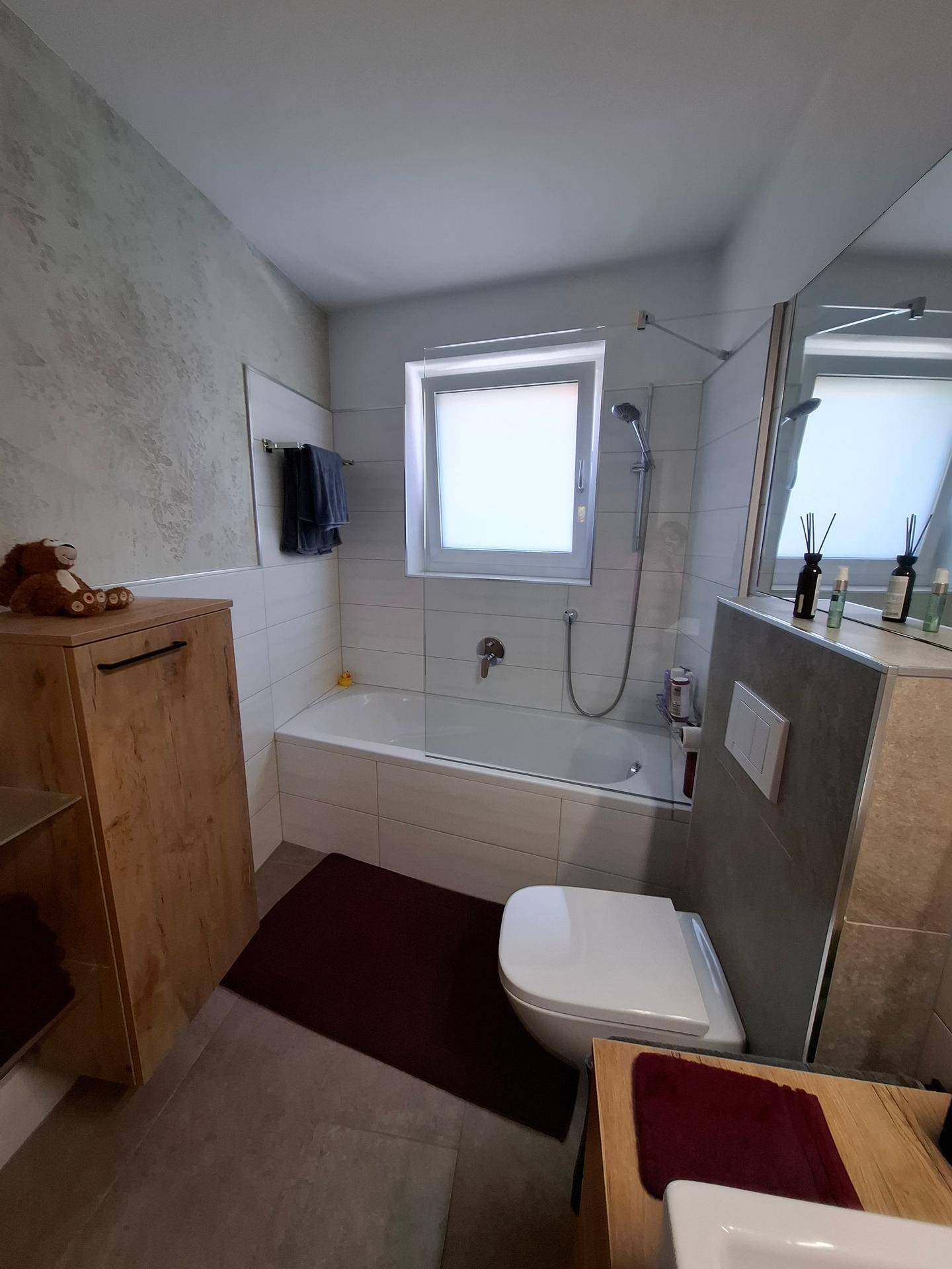 Modernes Badezimmer mit Badewanne, WC und Fenster, ausgestattet mit hellen Fliesen.