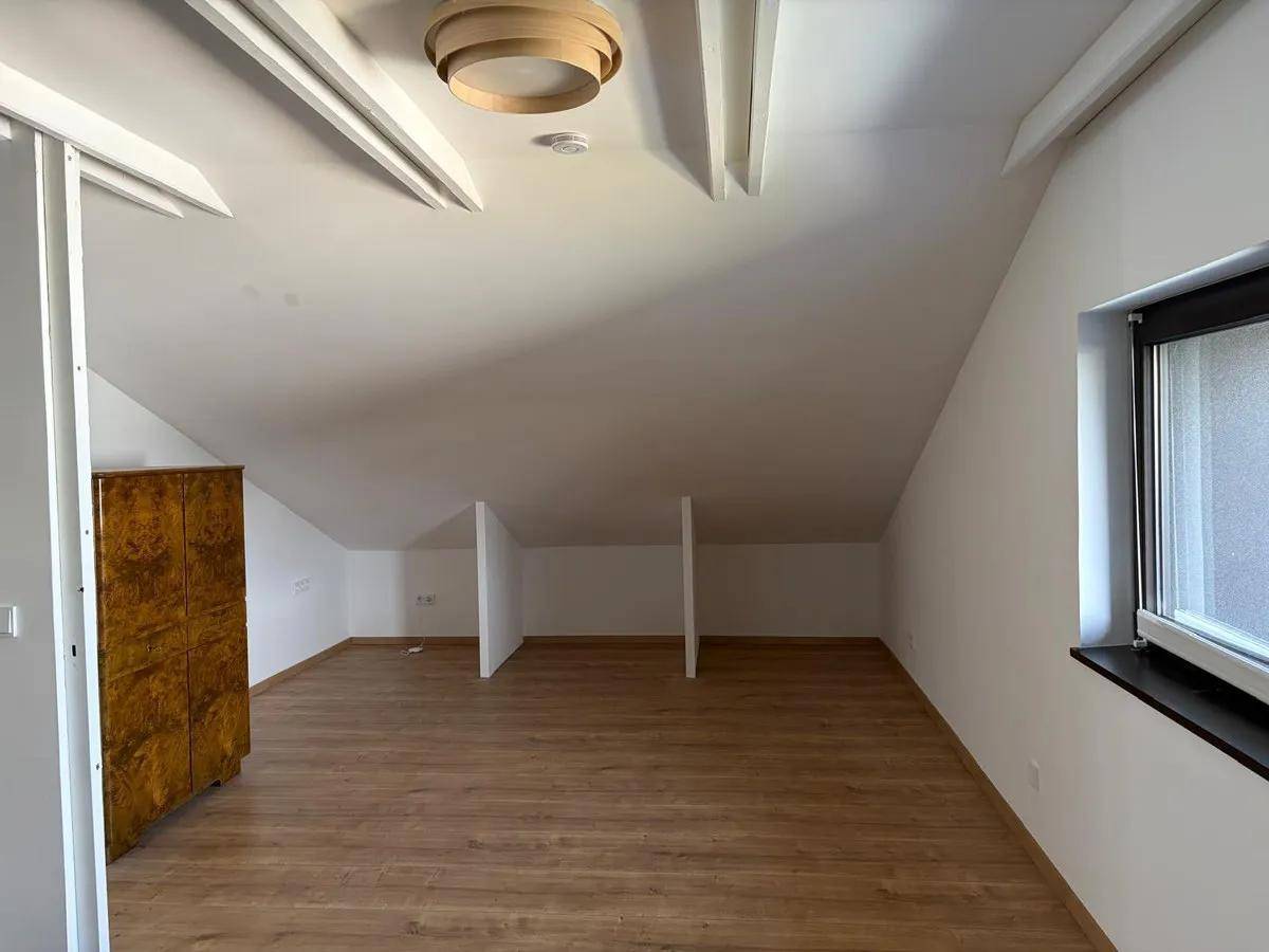 Heller Dachbodenraum mit schrägen Wänden, Laminatboden und einem Fenster für Tageslicht.