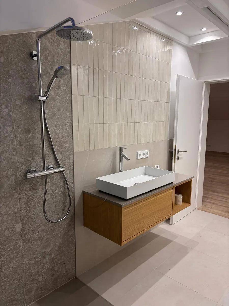 Helles Badezimmer mit moderner Dusche, schwebendem Waschtisch und beigen Fliesen.