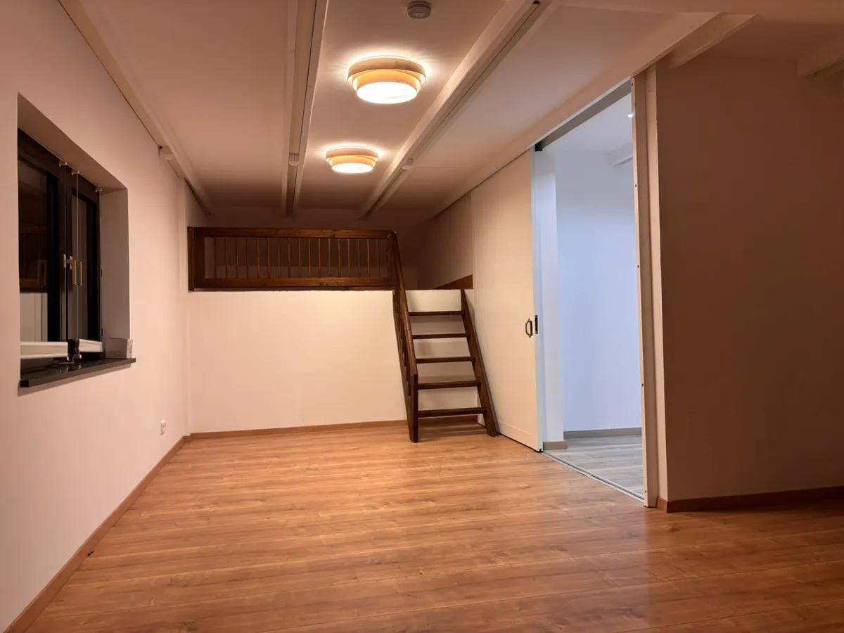 Heller Raum mit Laminatboden, Fenster und einer Holzleiter zu einer erhöhten Schlafebene.