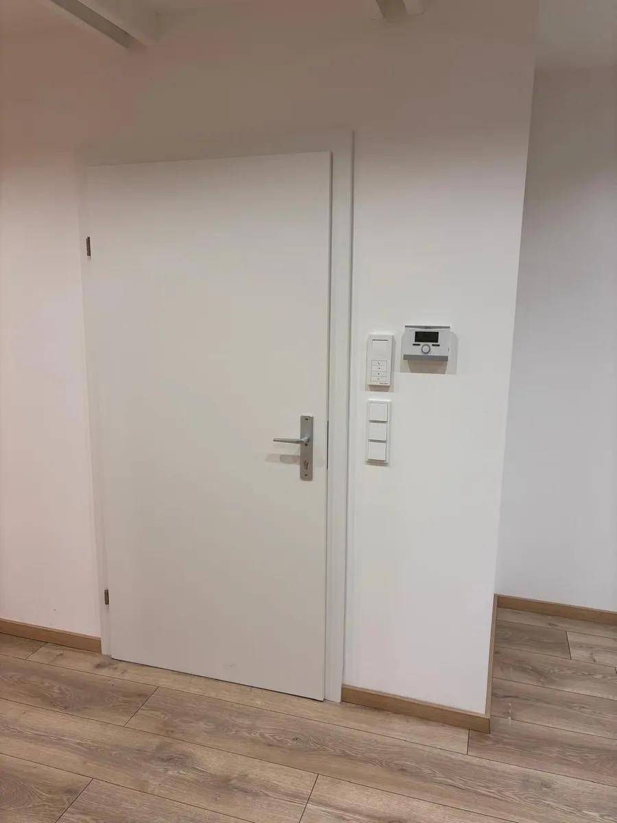 Weiße Tür in einem Flur mit Laminatboden und einem Wandthermostat.
