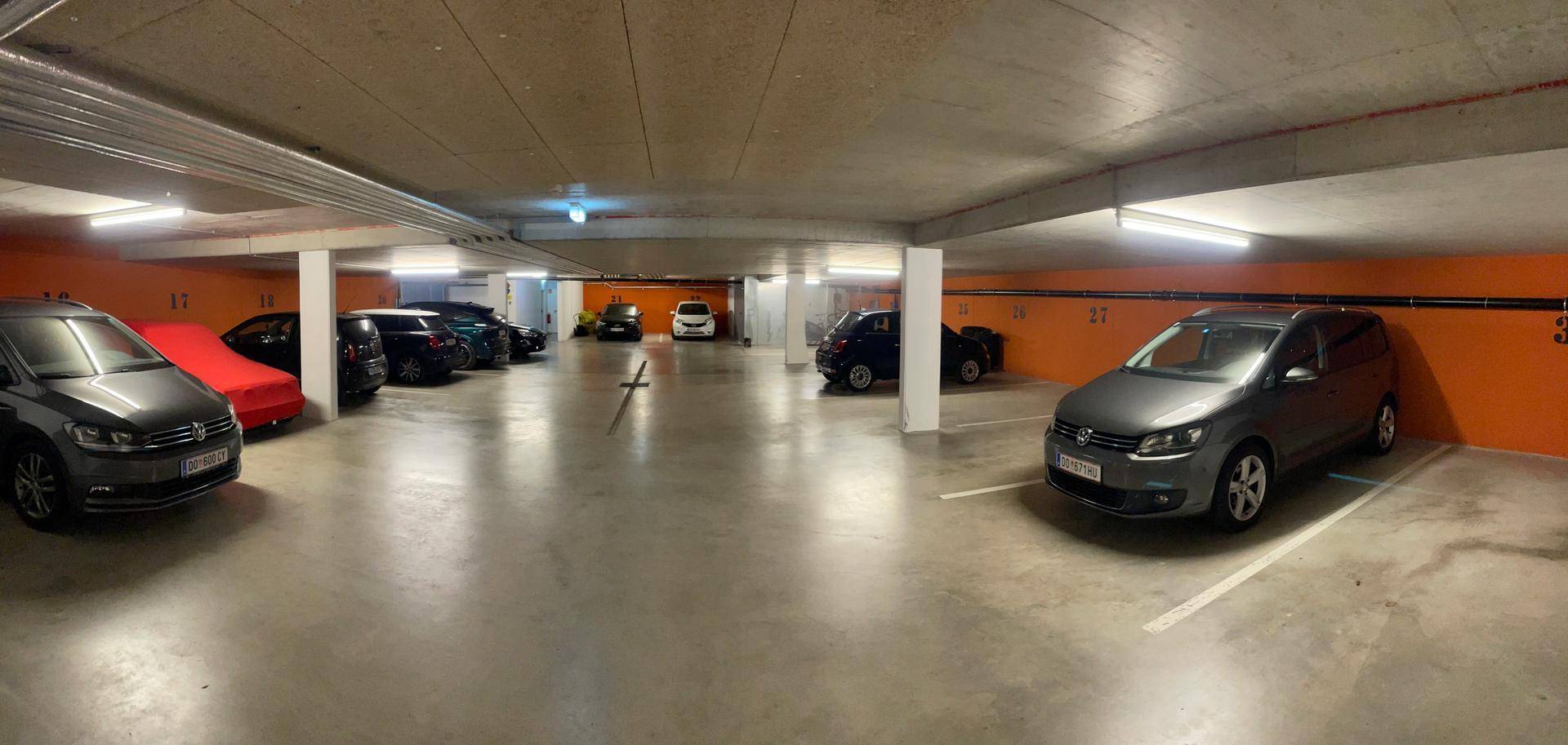Geräumige Tiefgarage mit mehreren geparkten Fahrzeugen und orangefarbenen Wänden.