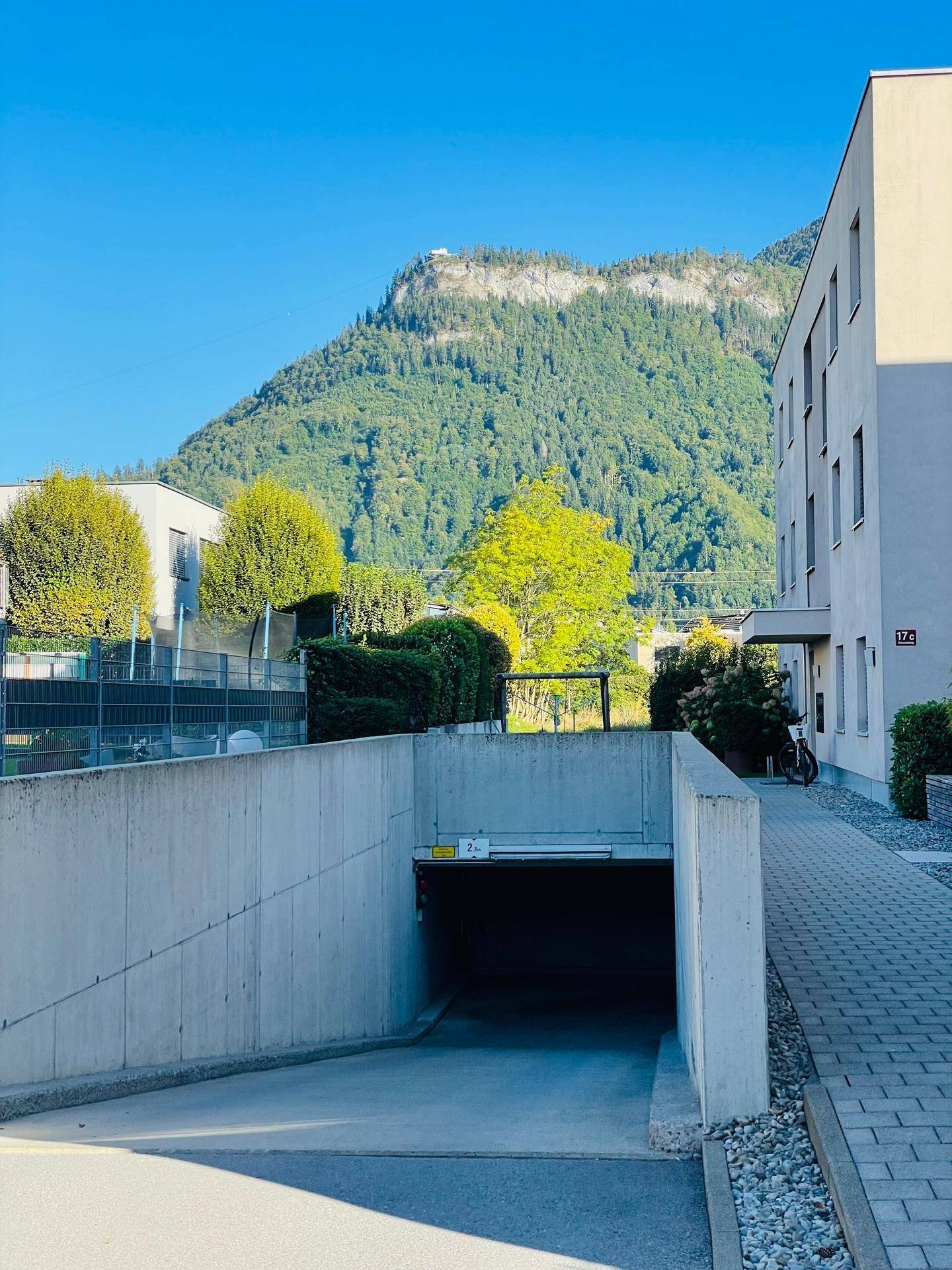 Zufahrt zur Tiefgarage eines modernen Wohngebäudes mit Bergkulisse im Hintergrund.