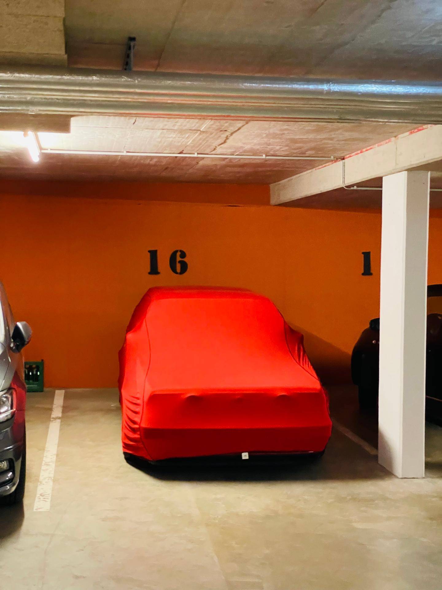 Ein Fahrzeug unter einer roten Abdeckung auf einem nummerierten Stellplatz in der Tiefgarage.