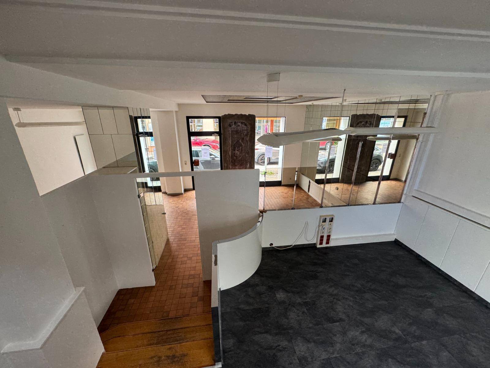 Gesamtansicht des Gewerberaums mit Treppe, Spiegelflächen und unterschiedlichen Bodenbelägen.