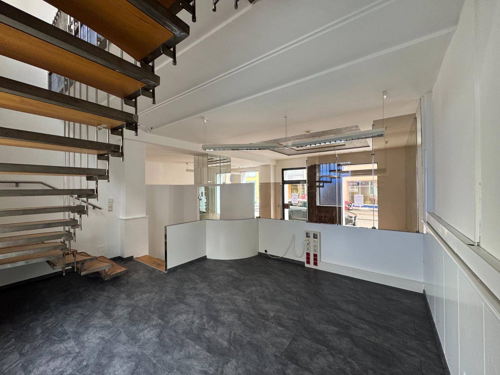 Geräumiger Gewerberaum mit dunklem Vinylboden, Treppe und Spiegelflächen, die den Raum erweitern.