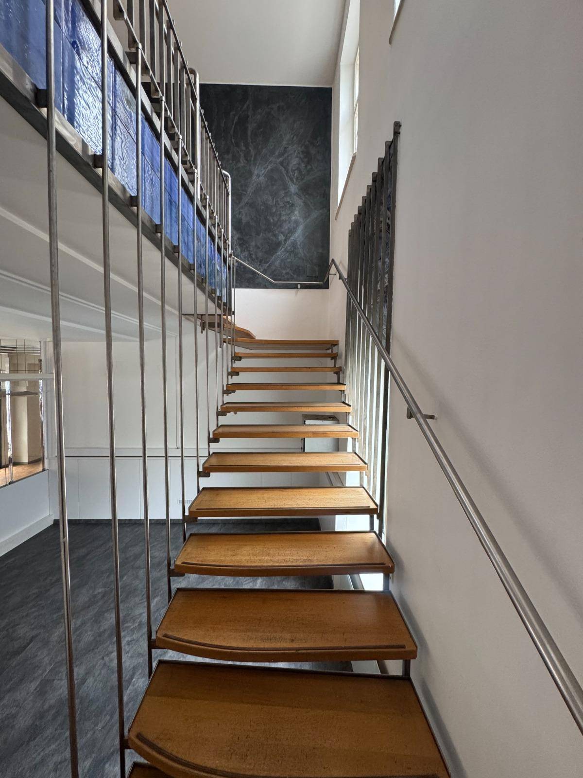 Moderne Holztreppe mit Metallgeländer, die zu einem oberen Stockwerk führt, mit viel Tageslicht.