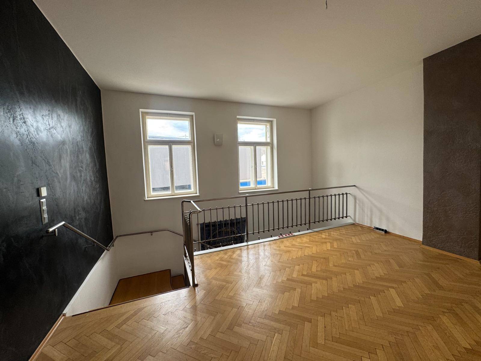 Obergeschoss mit Fischgrätparkett, dunkler Akzentwand und Blick auf die darunterliegende Treppe.