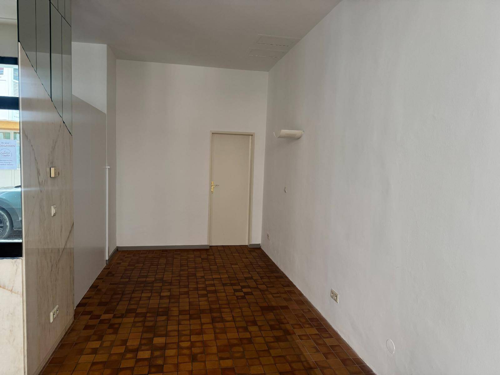 Leerer Gewerberaum mit weiß gestrichenen Wänden, gefliestem Boden und einer einfachen Tür.
