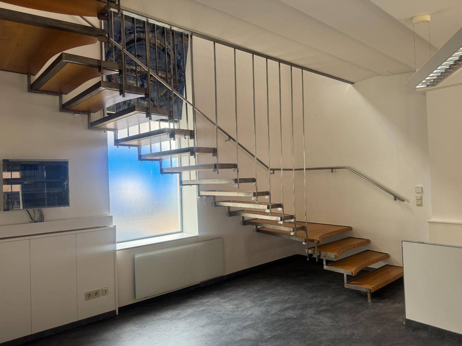 Moderne Holztreppe mit Metallgeländer und einem großen Fenster, das den Raum mit Licht füllt.