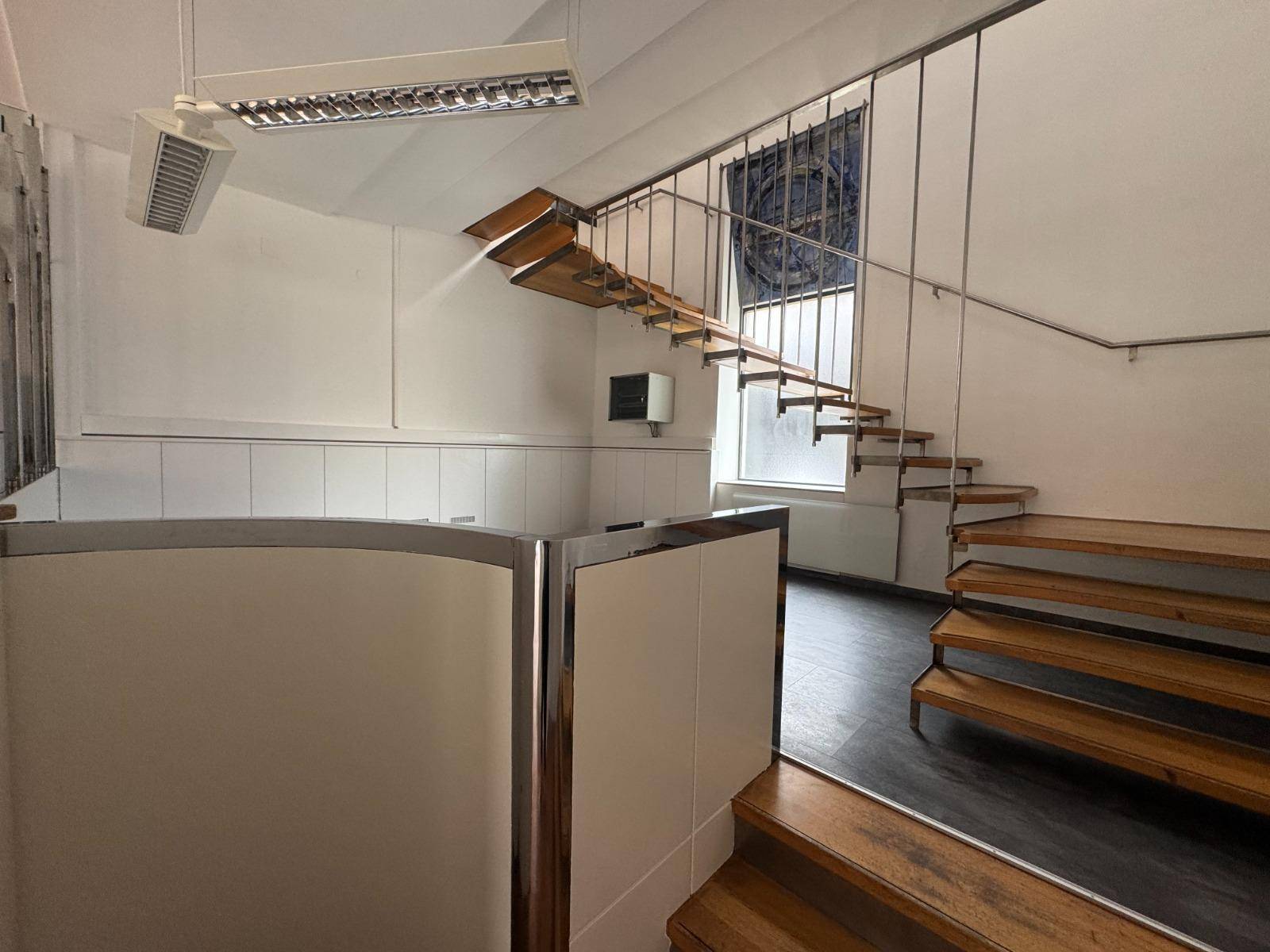 Innenansicht eines Gewerberaums mit Treppe, die zu einer oberen Ebene führt, und einem Empfangsbereich.
