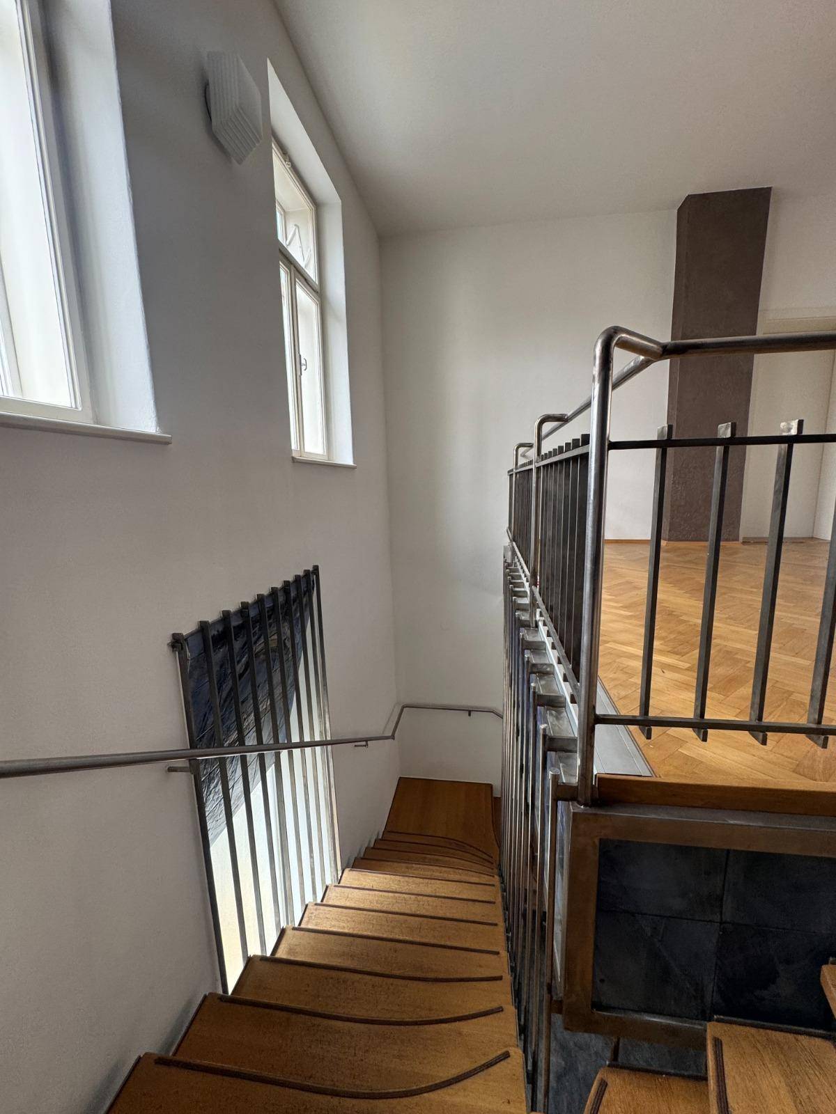 Blick von oben auf die Holztreppe mit Metallgeländer und Fenstern, die Tageslicht hereinlassen.