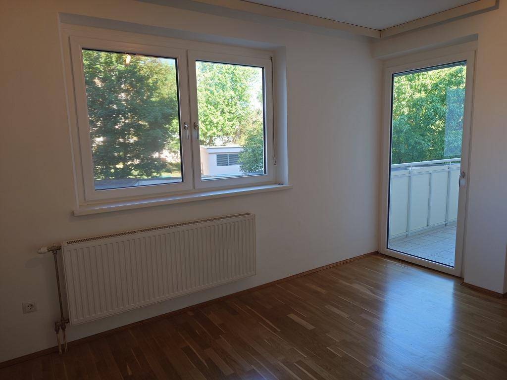 Helles Wohnzimmer mit Parkettboden und großen Fenstern, die viel Tageslicht hereinlassen.