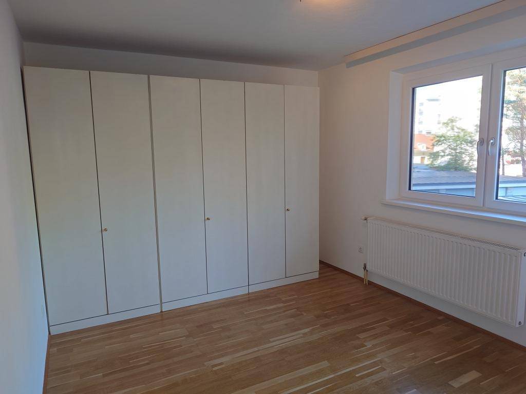Schlafzimmer mit Parkettboden, Einbauschränken und einem großen Fenster für viel Tageslicht.