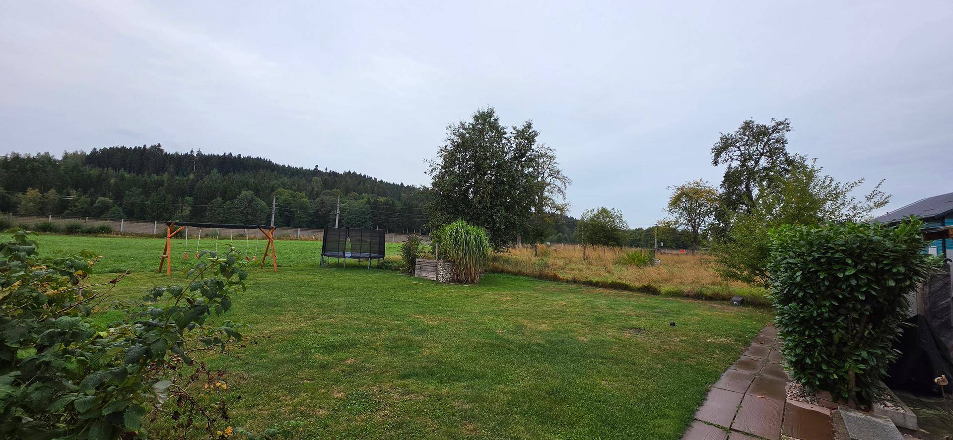 Weitläufiger Garten mit Bäumen, Rasen und Blick auf die umliegende Natur.