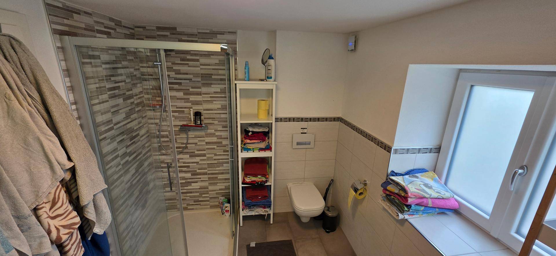 Modernes Badezimmer mit Duschkabine, WC und Fenster für Tageslicht.